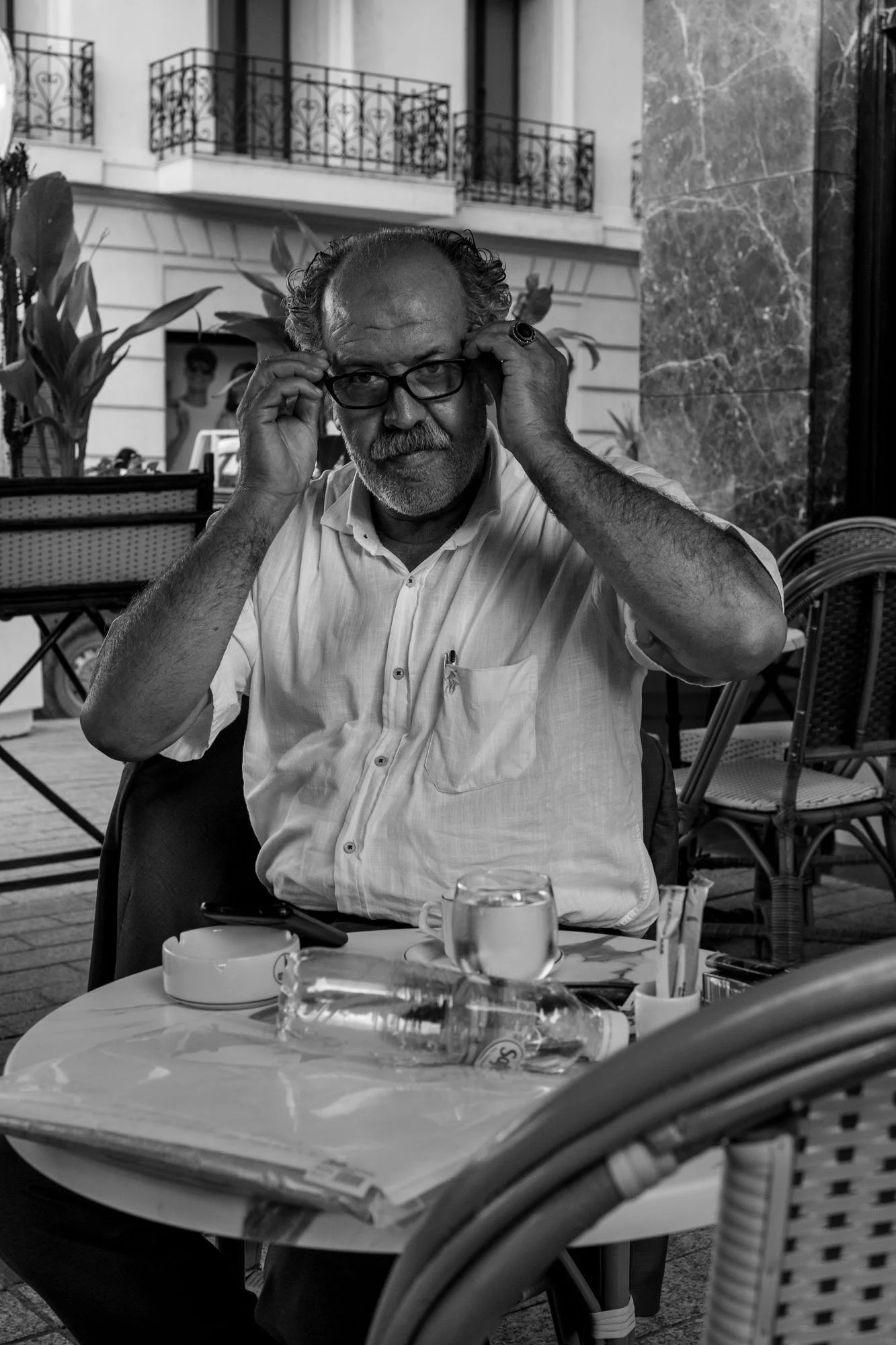  Man adjusting his glasses at a café terrace, Tunis. Black-and-white street portrait by Chris Perona. 