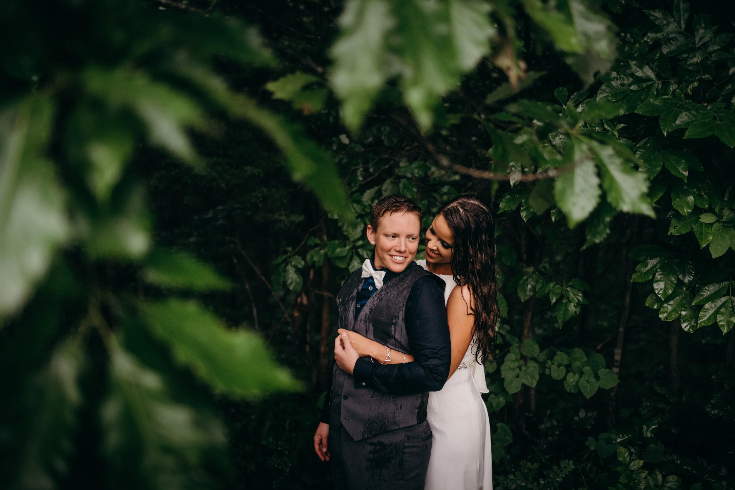 smiling woman in suit with her wife hugging her from behind