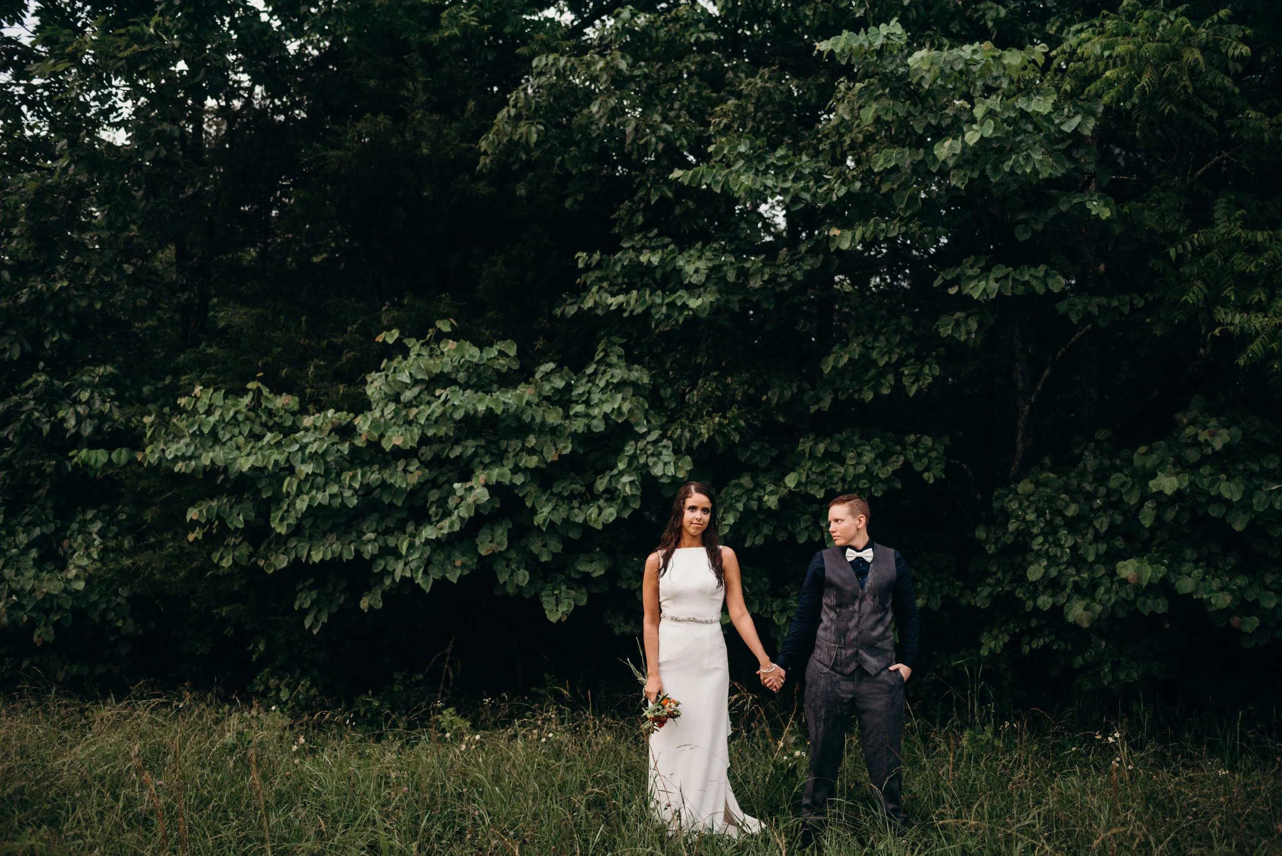 newly married same-sex couple holding hands in a field after rainstorm