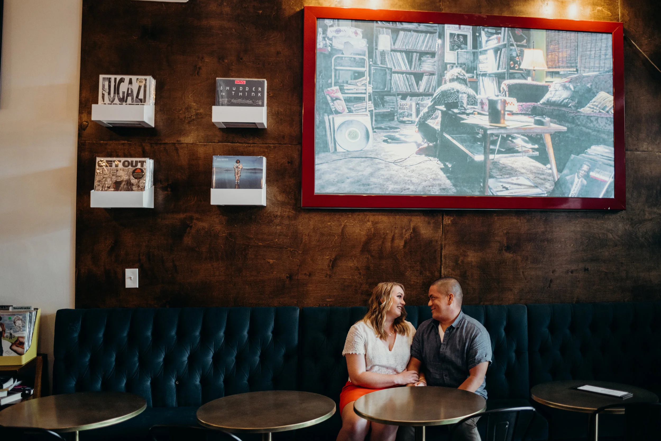 engaged couple sitting in cafe at Songbyrd Cafe and Record Store with art and records behind them