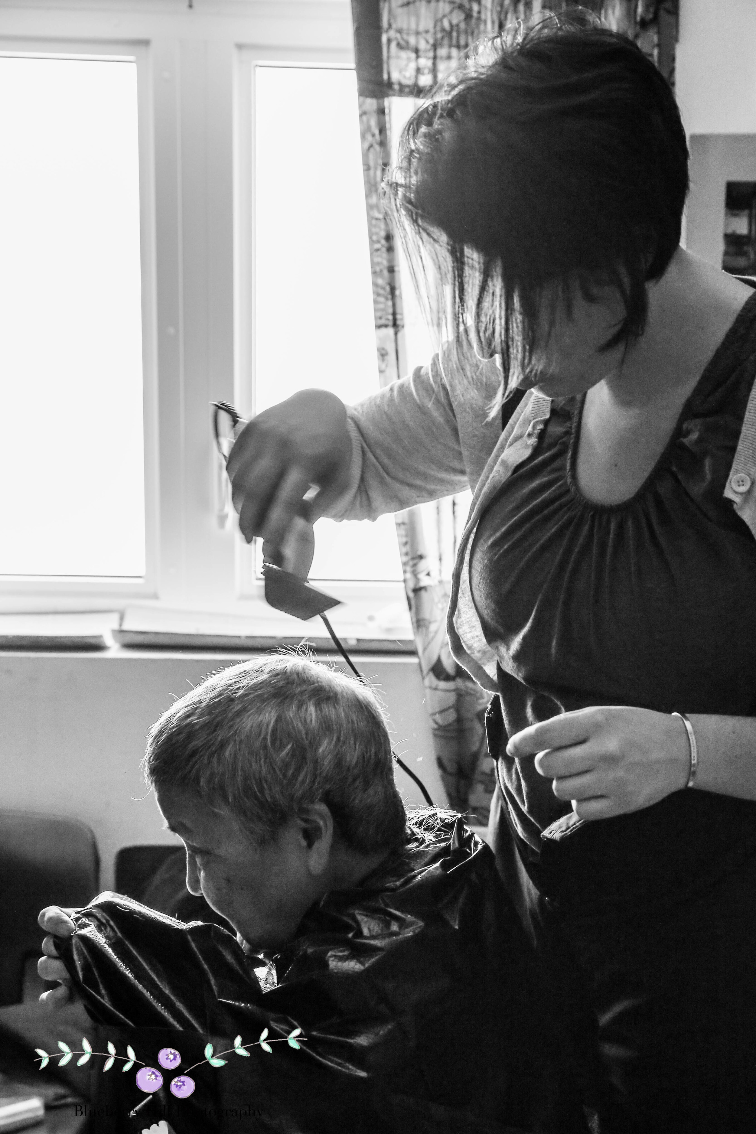 Lena sits in her kitchen, wrapped in a trash bag, while Bethany cuts her hair.