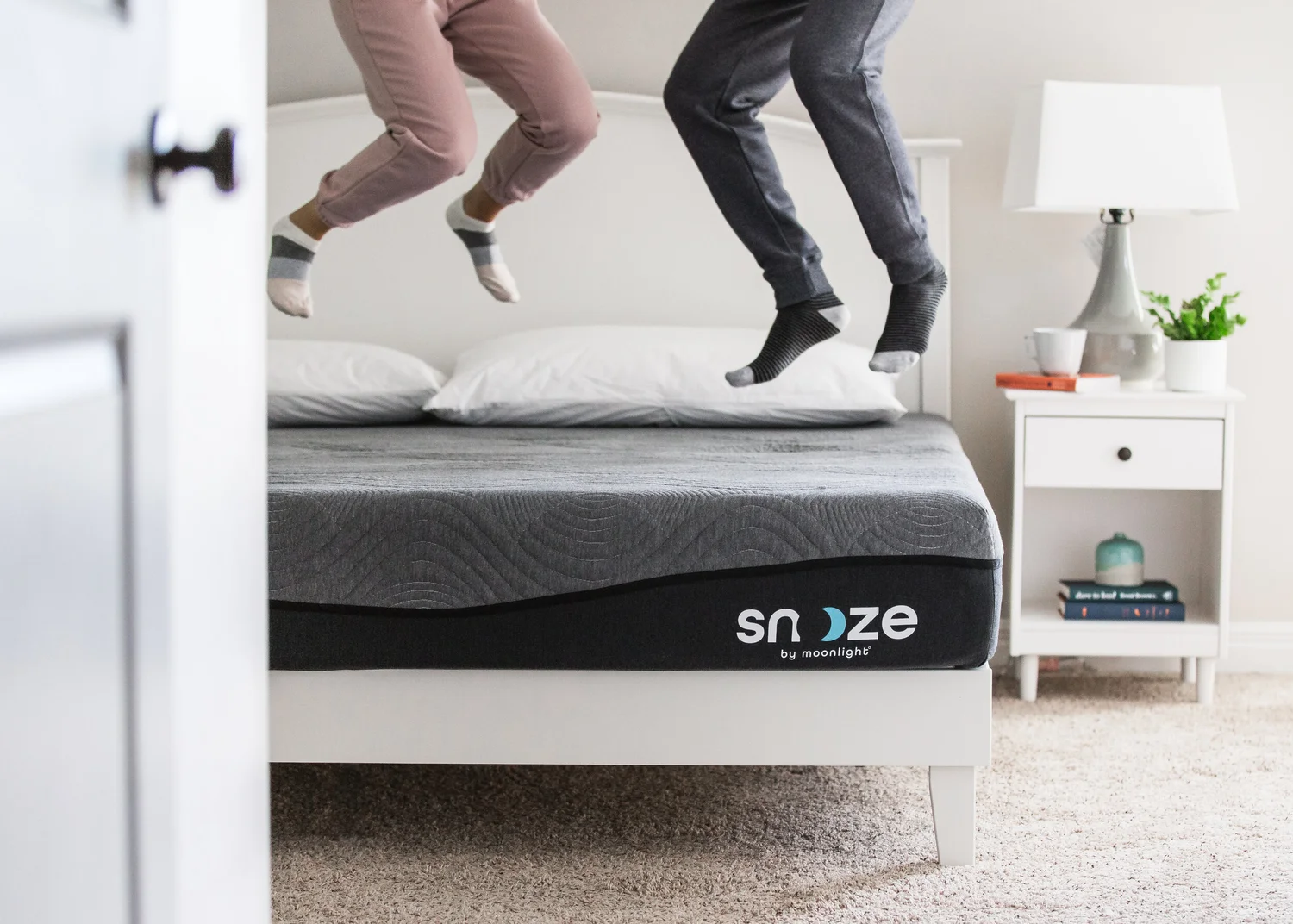 Playful lifestyle photography of two people jumping on a Snooze mattress