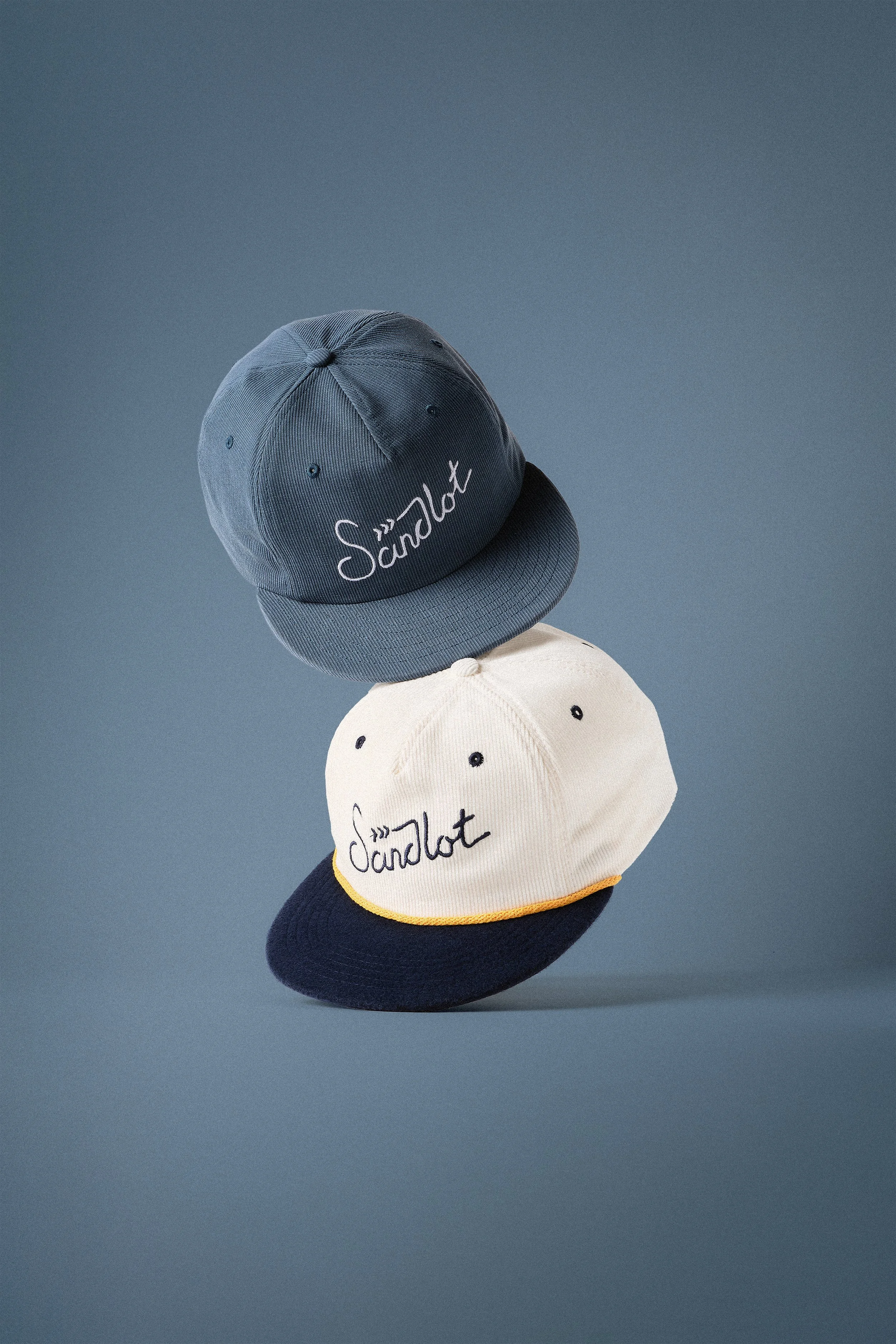 Sandlot Goods navy and cream script snapbacks floating on blue - studio hat photography