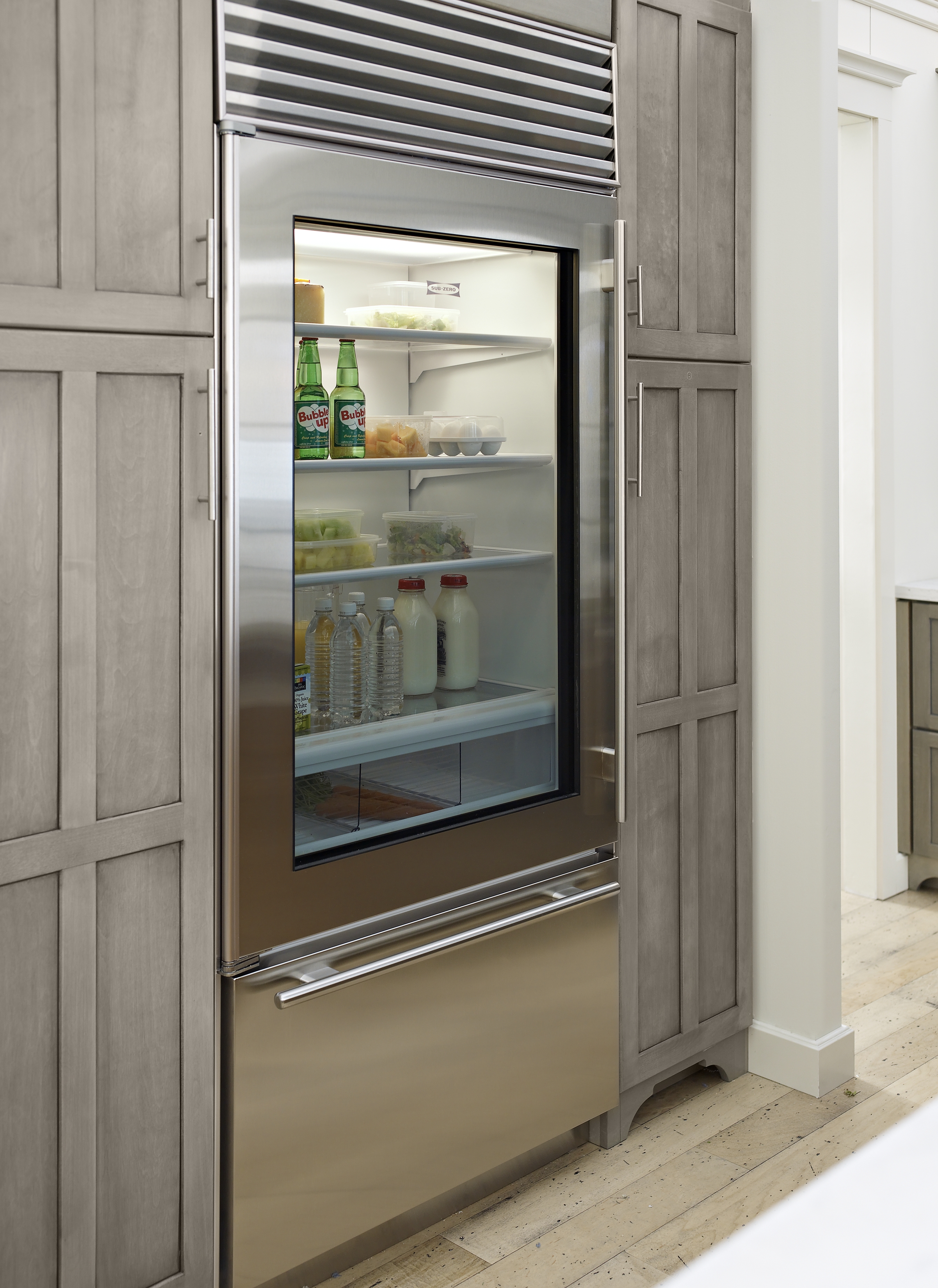 Stainless steel fridge fitted between wooden cabinetry along the kitchen wall