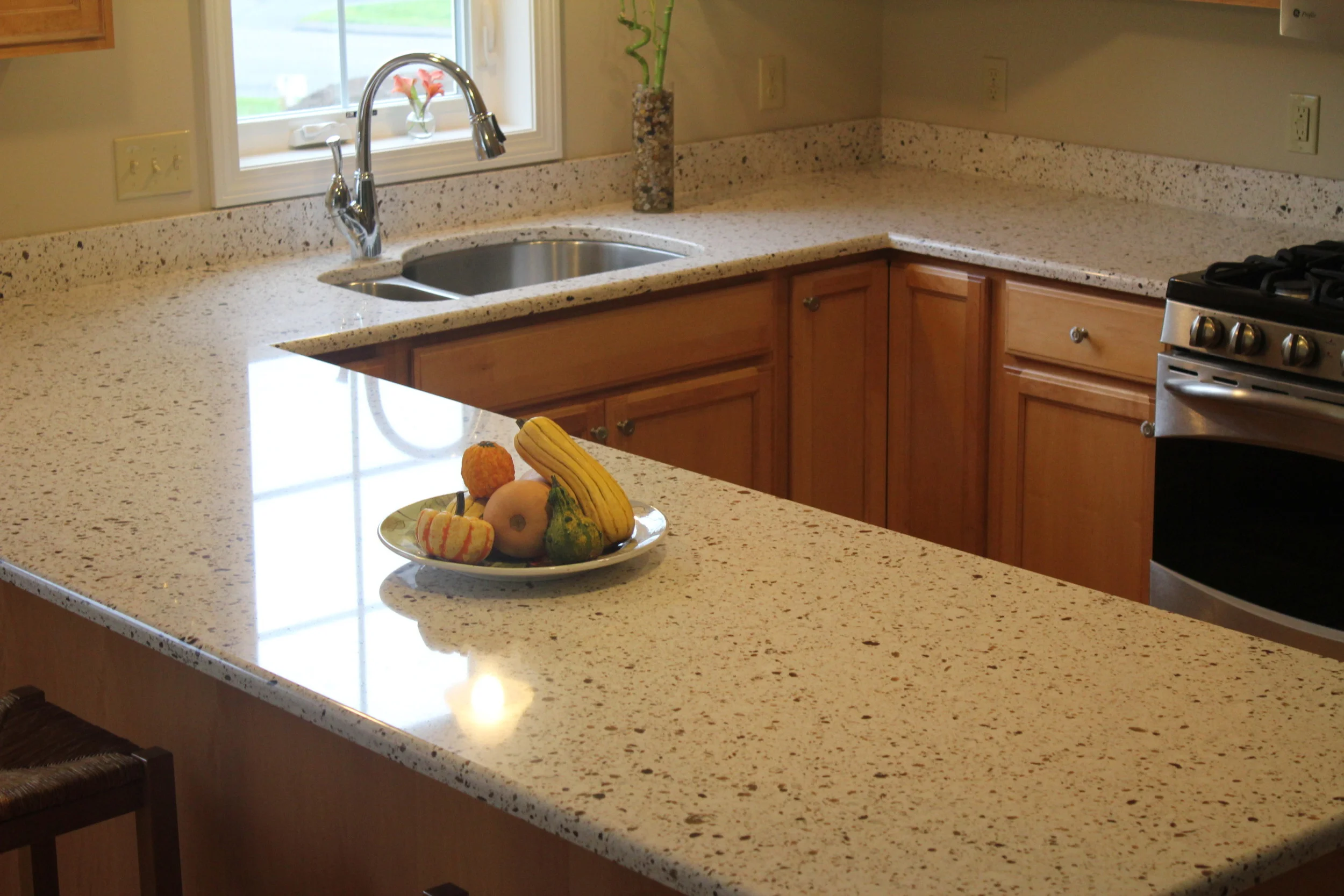 A U shaped kitchen with light Walnut cabinetry and speckled white granite countertop