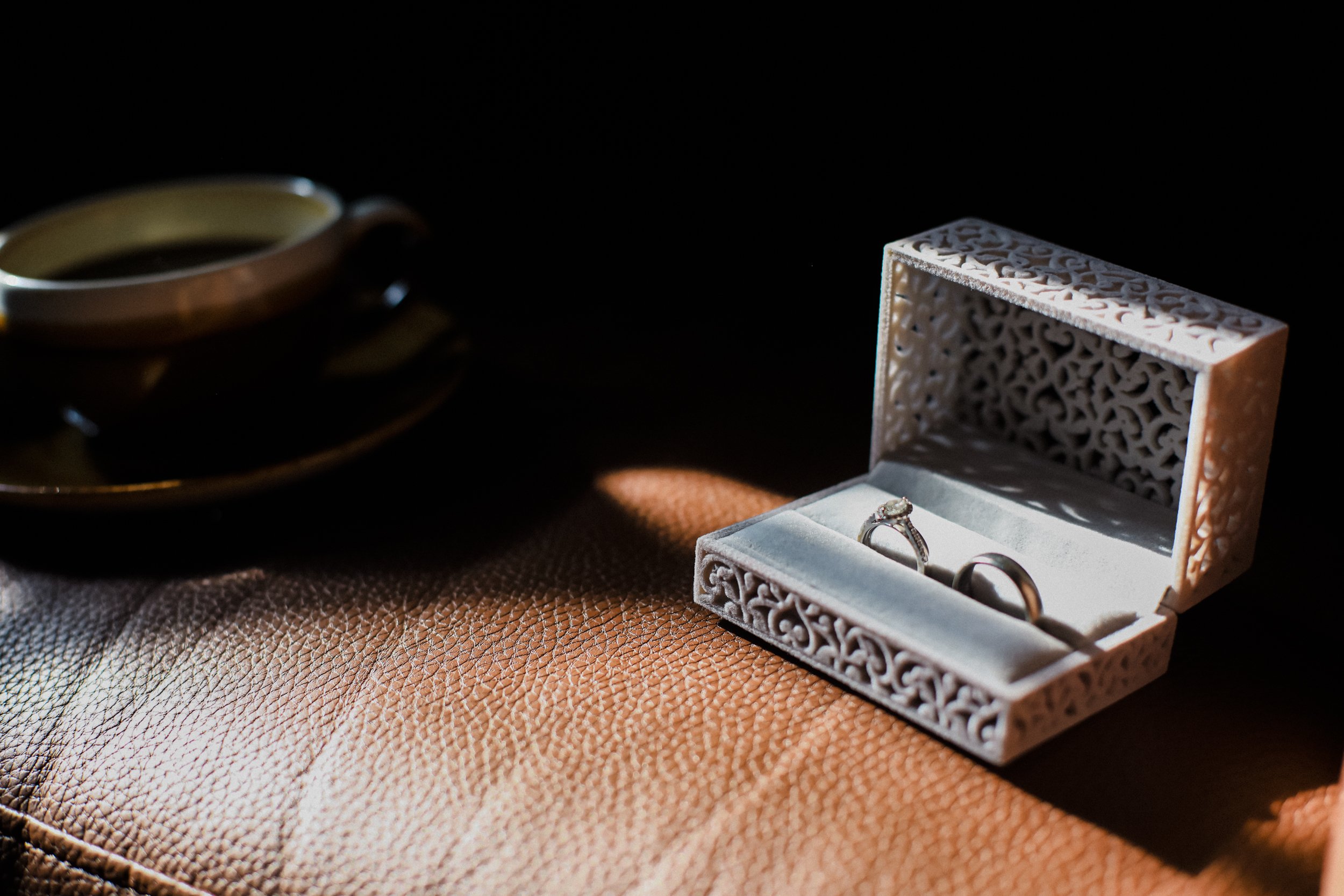 Symbolic Elegance: Wedding Rings Rest Inside a Wedding Ring Box, Placed on a Luxurious Brown Leather Chair in the Titanic Hotel Room, Creating a Scene of Timeless Beauty.