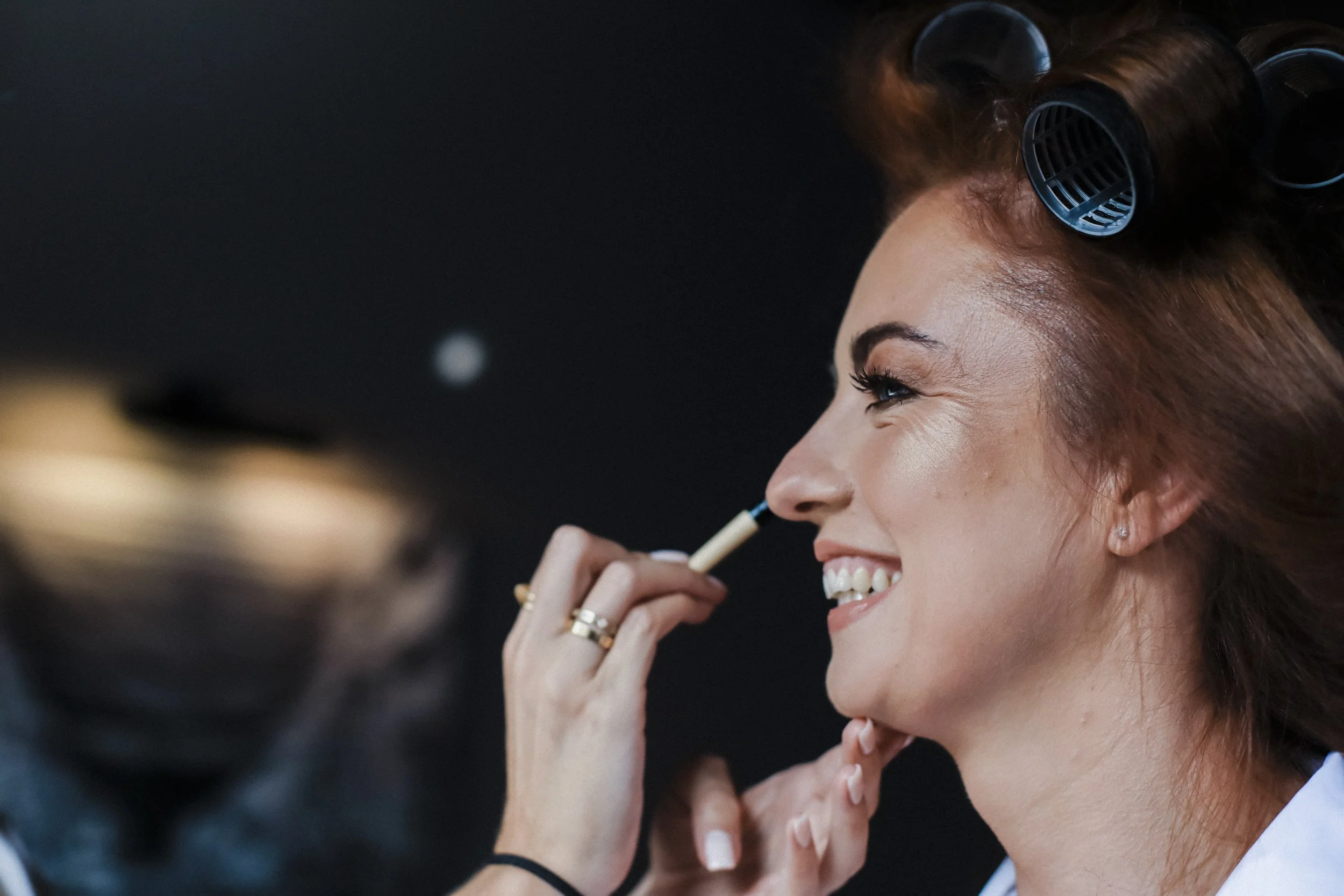 Radiant Joy: Bride Smiles with Elegance as She Gets Her Makeup Done in Liverpool's Titanic Hotel, Capturing a Moment of Delight Amidst the Wedding Preparations.