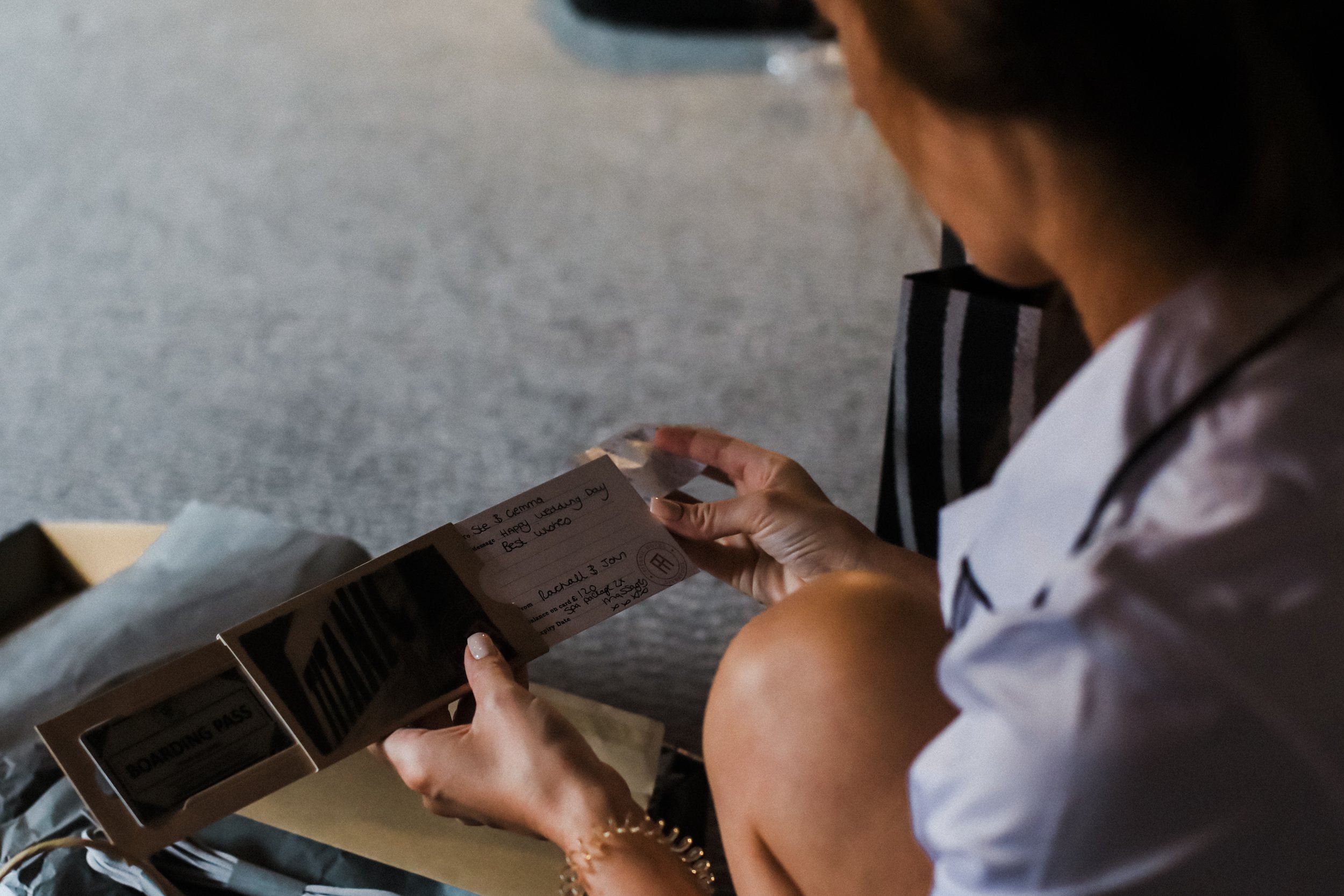 Gift of Relaxation:  The Bride Crouches Down with Delight, Admiring Her Wedding Gift of a Spa Package at Titanic Hotel, Creating a Moment of Appreciation and Excitement.