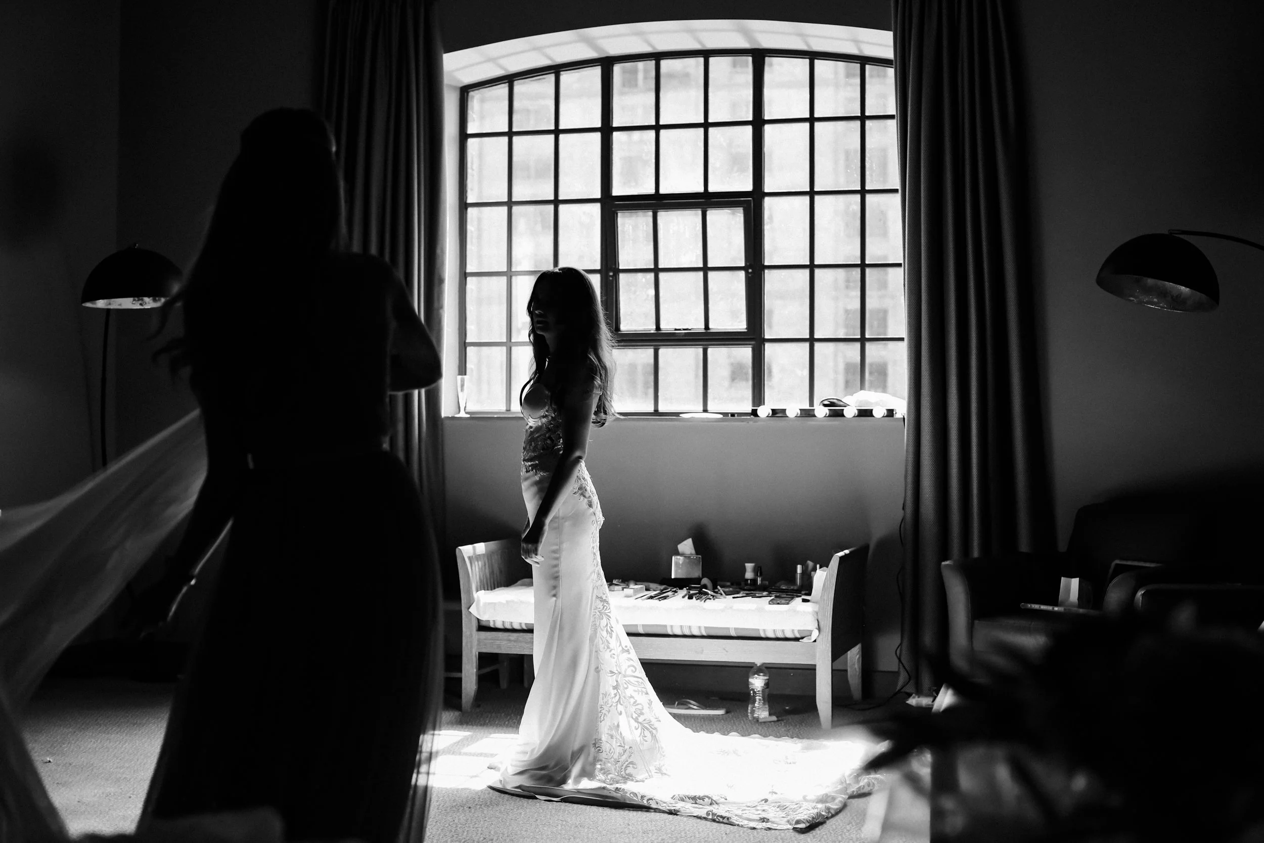 Bathed in Light: Bride Stands Before a Window at Titanic Hotel, Embracing the Natural Light in a Captivating Moment of Radiance