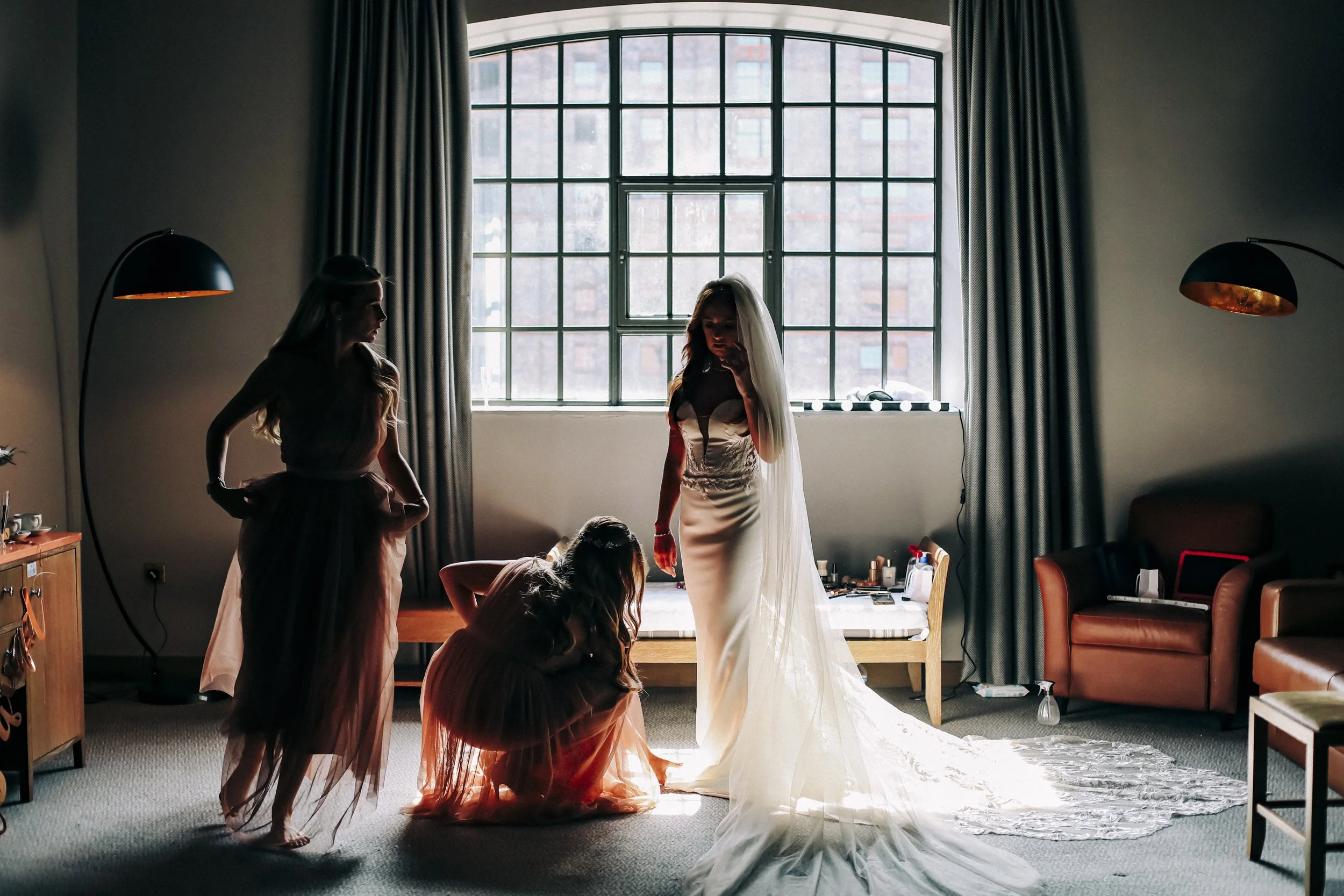 Bridesmaids Assisting Bride: Candid Moment by Window at Titanic Hotel Liverpool