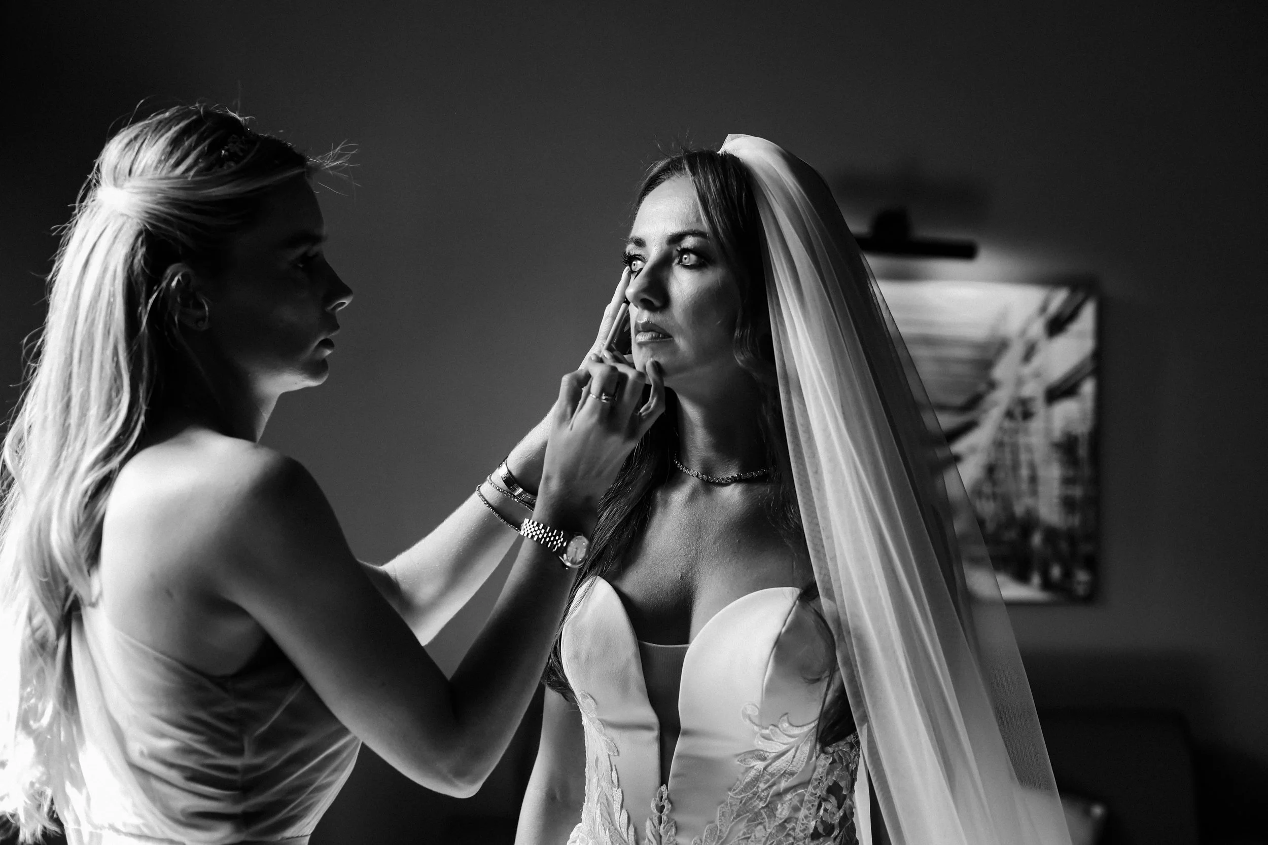 uminous Beauty: Bride Glows in the Light Streaming Through the Window at Titanic Hotel as Bridesmaid Adds Final Touch-Ups to Makeup, Creating a Picture of Radiant Elegance.