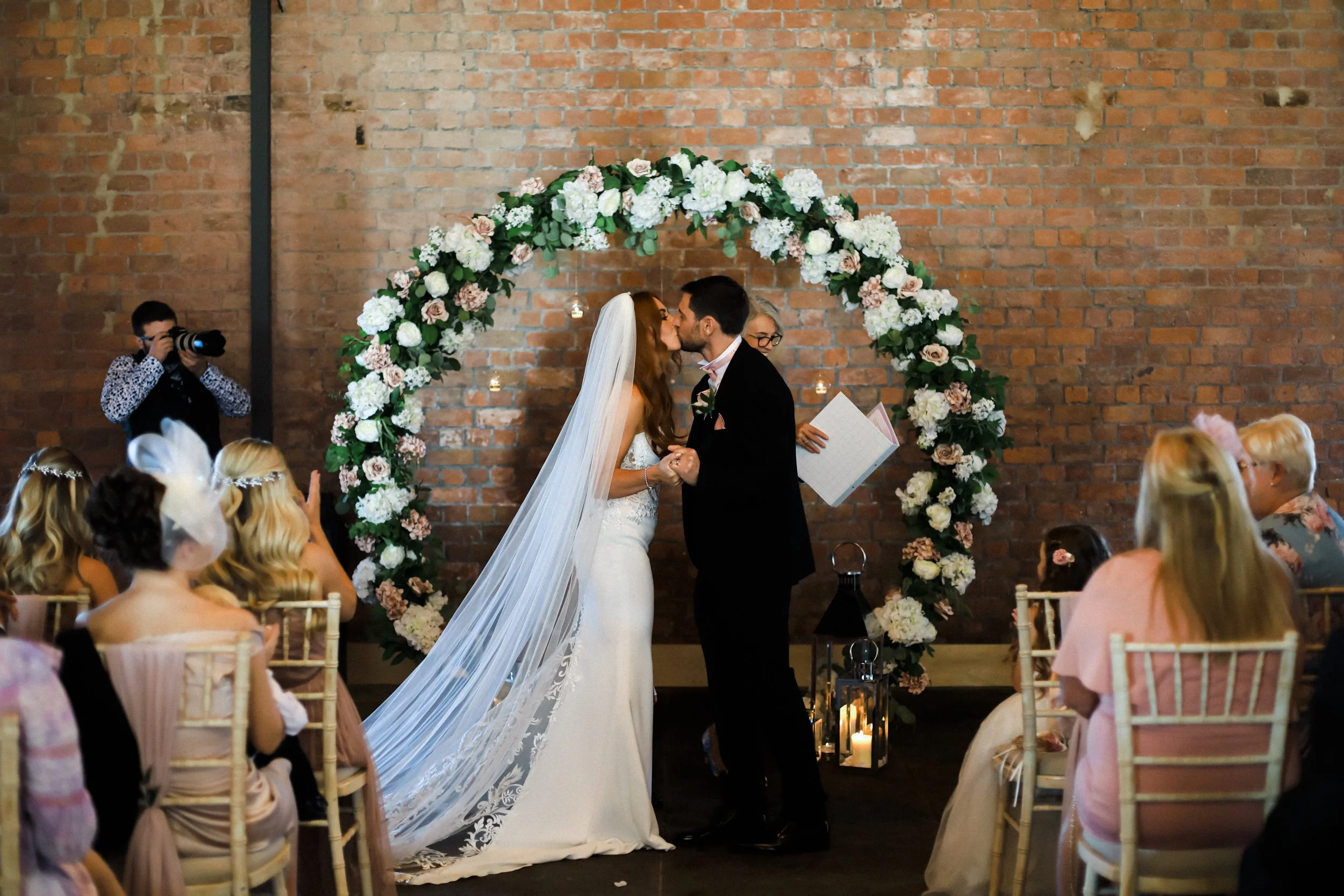 Sealing Their Love: Bride and Groom Share a Heartfelt Kiss During Their Ceremony at Titanic Hotel, Cementing Their Commitment to Each Other in a Tender Moment.