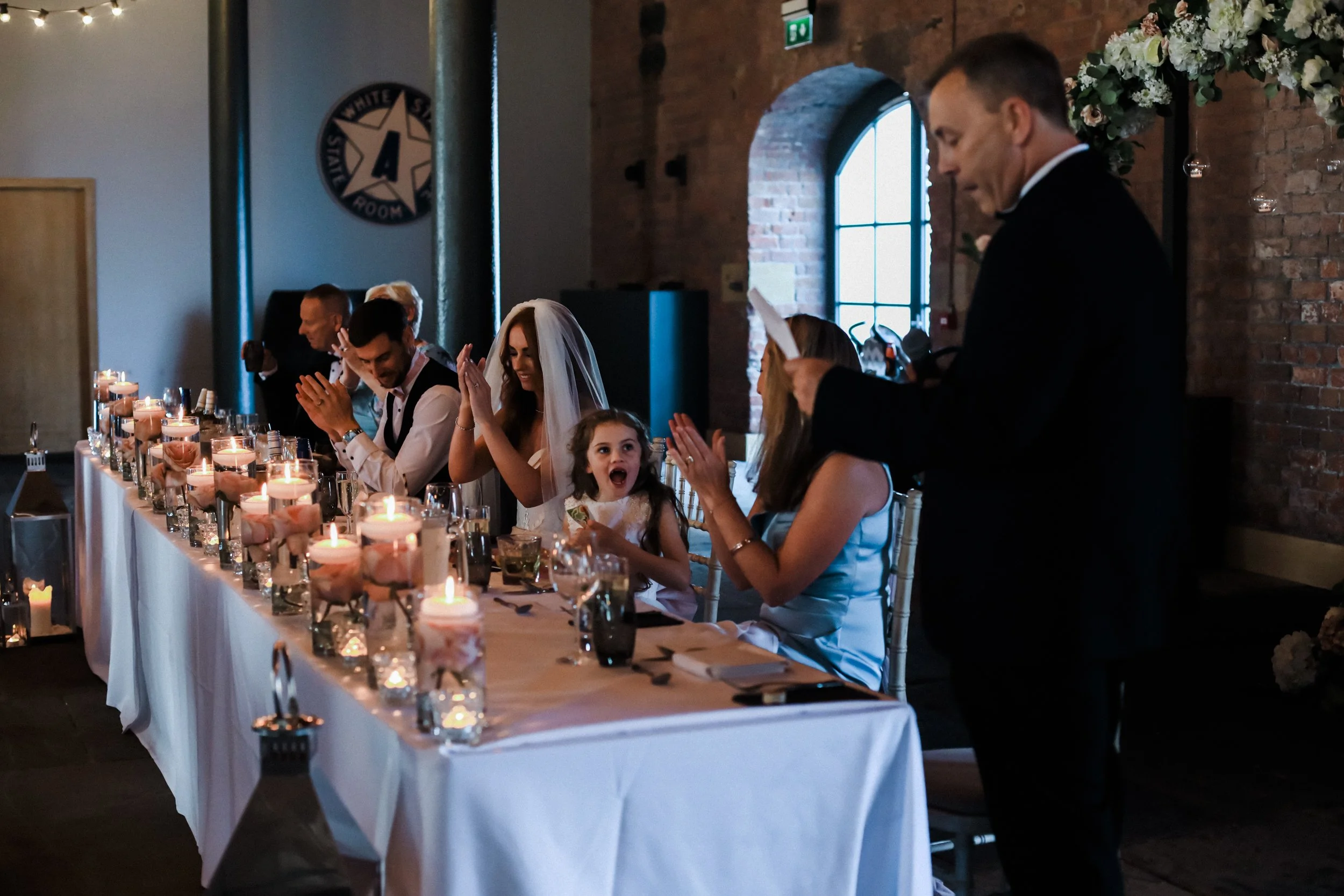 Enthusiastic applause resonates amidst ongoing speeches at the exquisite Titanic Hotel Liverpool wedding celebration.