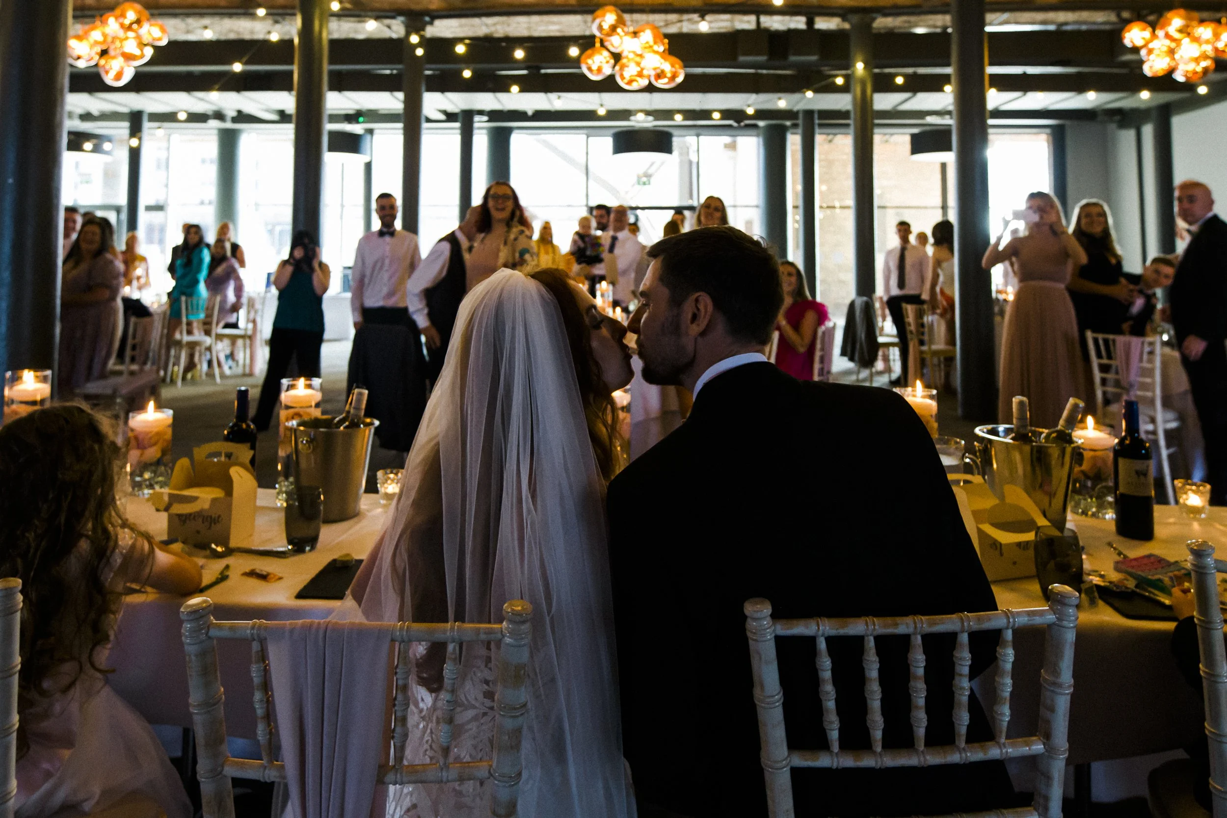 Romantic Moment: A Kiss Shared Between the Bride and Groom at the Wedding Breakfast, Captured from Behind, Adding an Intimate and Affectionate Touch to Their Titanic Hotel Liverpool Wedding.
