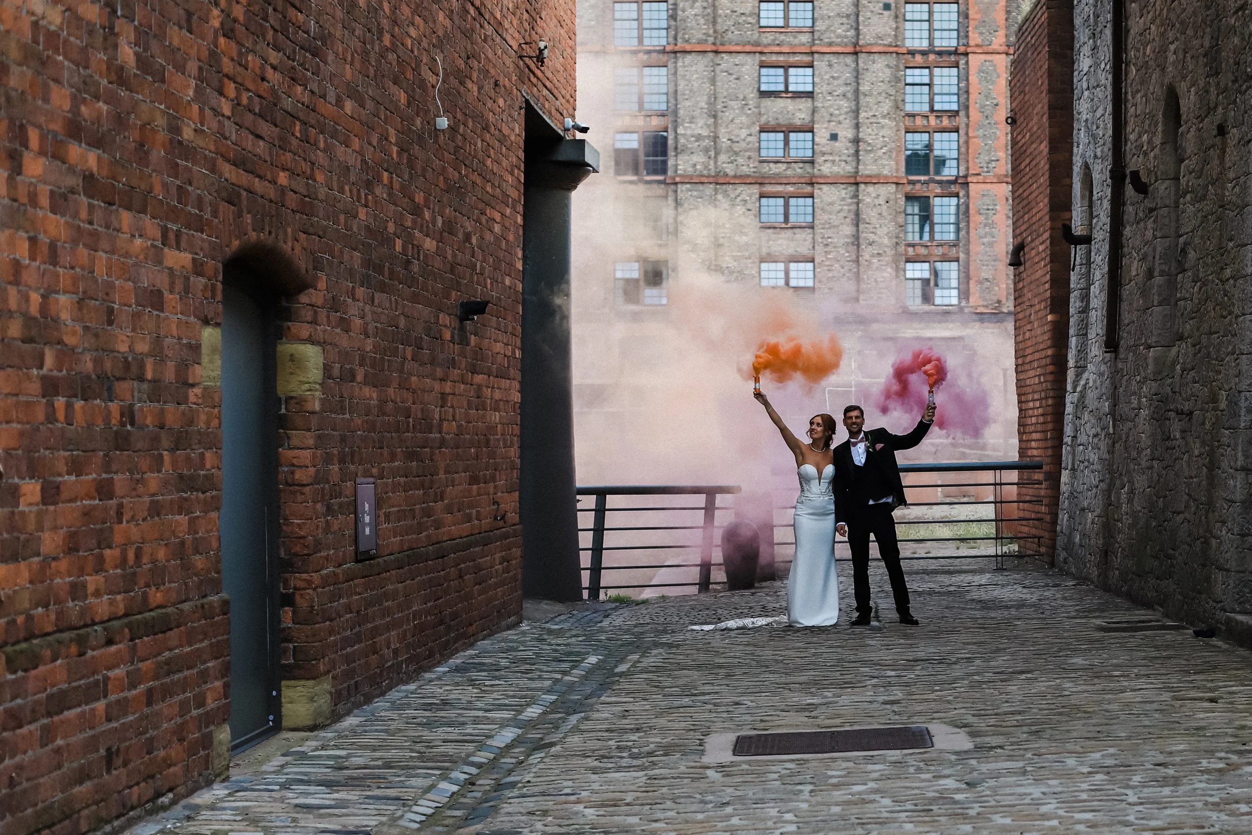 Vibrant Celebration: Bride and Groom Add a Splash of Colorful Fun with Pink and Orange Smoke Bombs at Titanic Hotel, Creating a Playful and Festive Atmosphere.