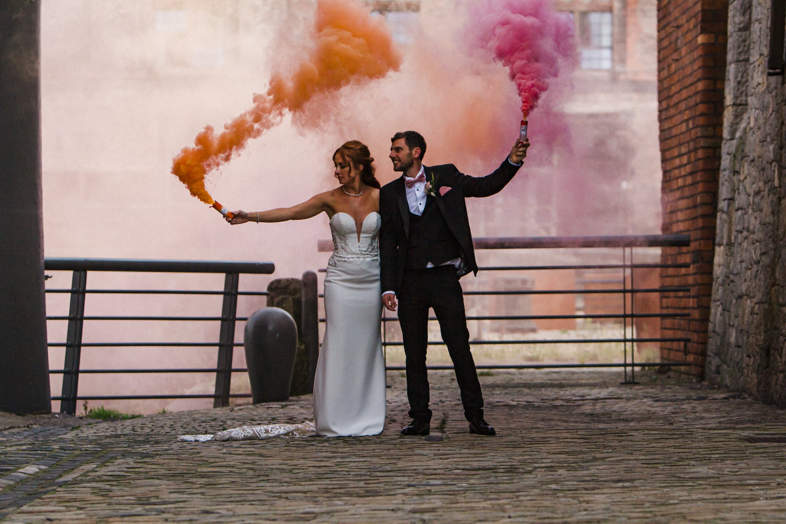Vibrant Celebration: Bride and Groom Add a Splash of Colorful Fun with Pink and Orange Smoke Bombs at Titanic Hotel, Creating a Playful and Festive Atmosphere.