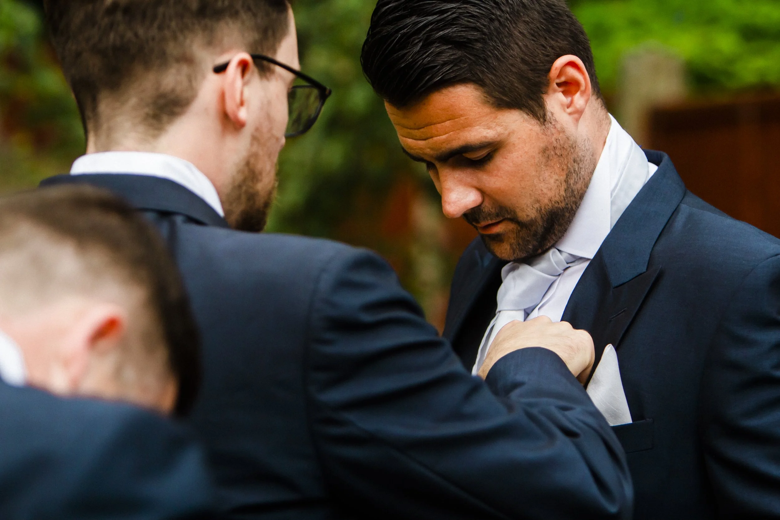 Teamwork in Style: Groomsmen Collaborate to Ensure Every Detail of Another Groomsman's Suit Is Perfect at the Brook Hall Wedding. 
