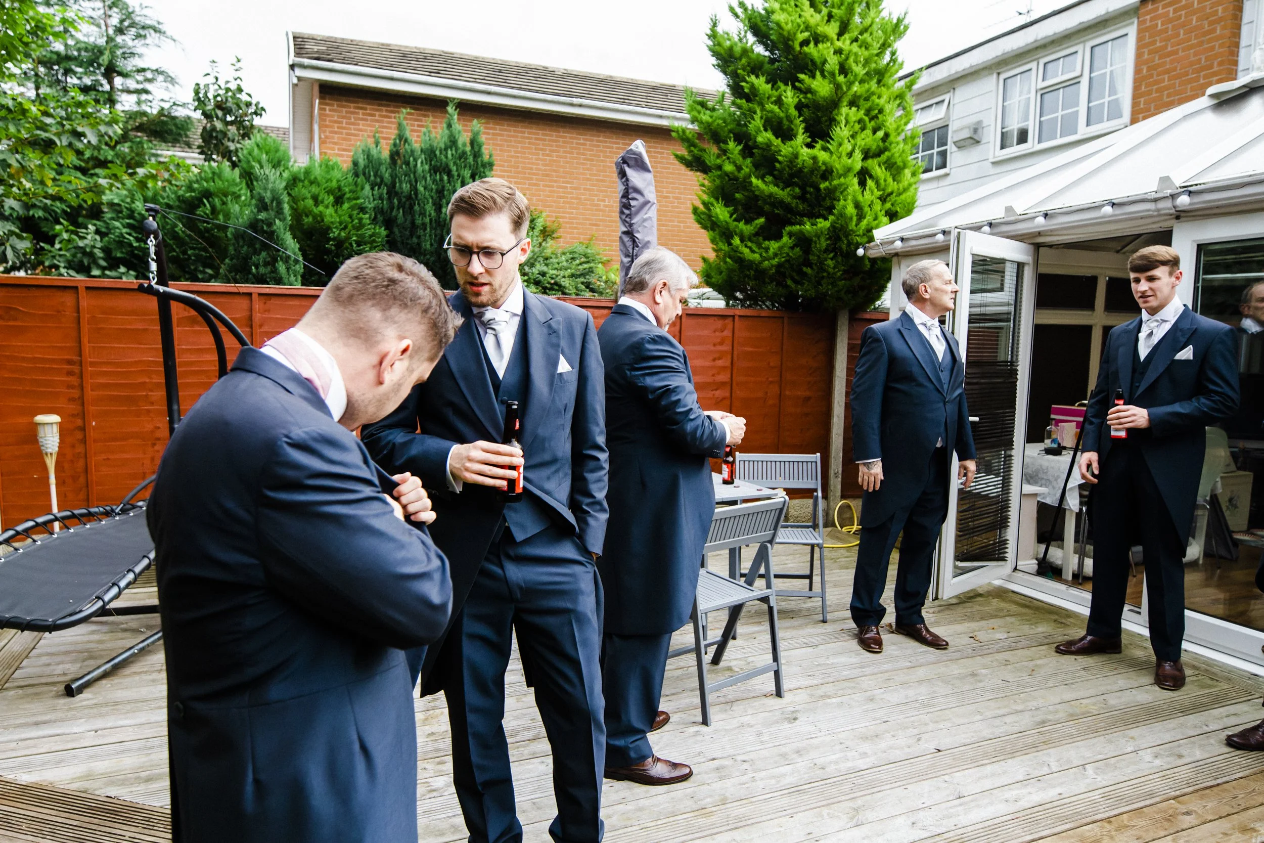 Sunny Refreshment: The Groom and His Groomsmen Enjoy Some Drinks in the Warm Sunshine, Creating a Relaxed and Enjoyable Atmosphere Captured by the Brook Hall Hotel Wedding Photography.