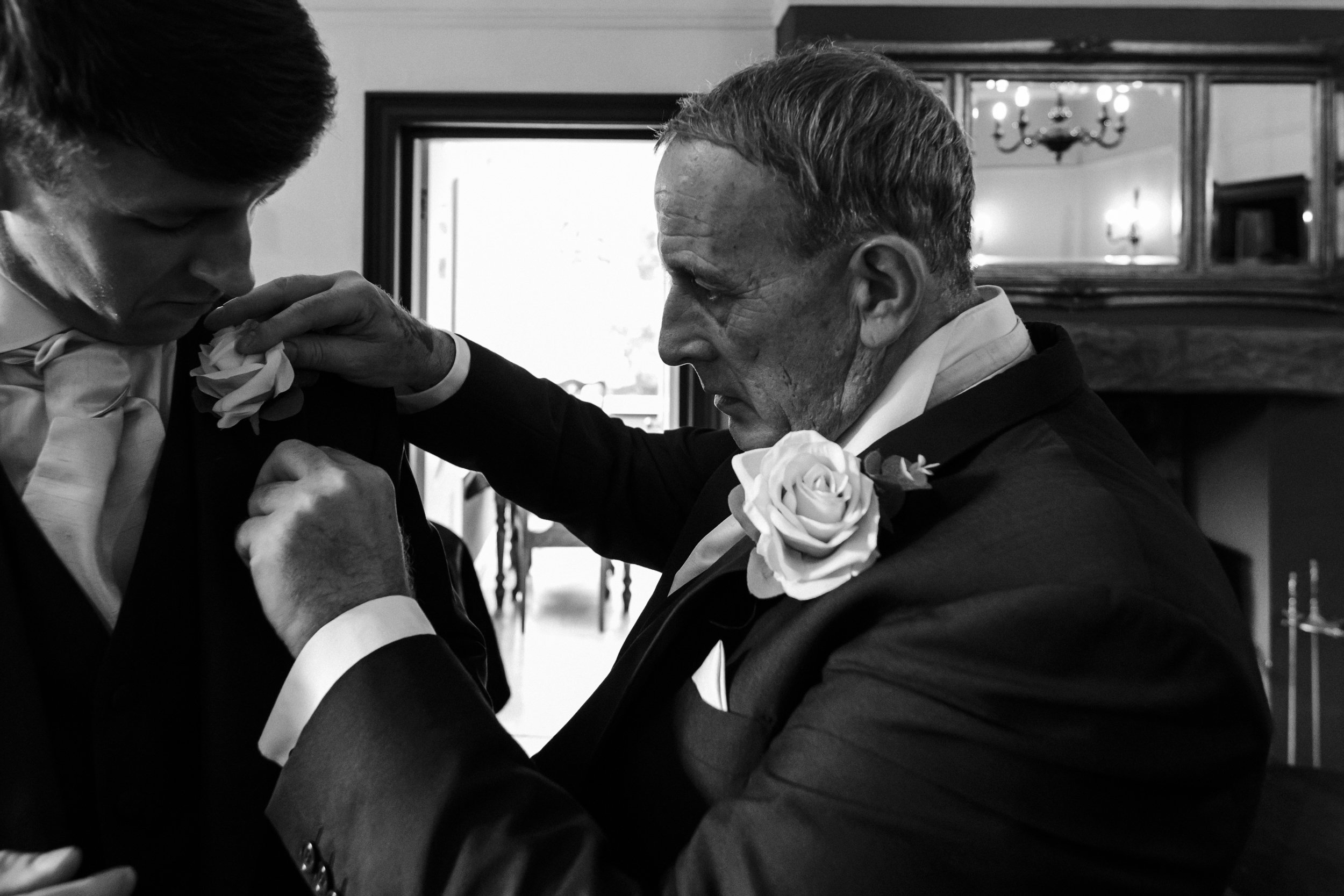 father of the bride helping a groomsman with his suit Brook Hall wedding photographer 