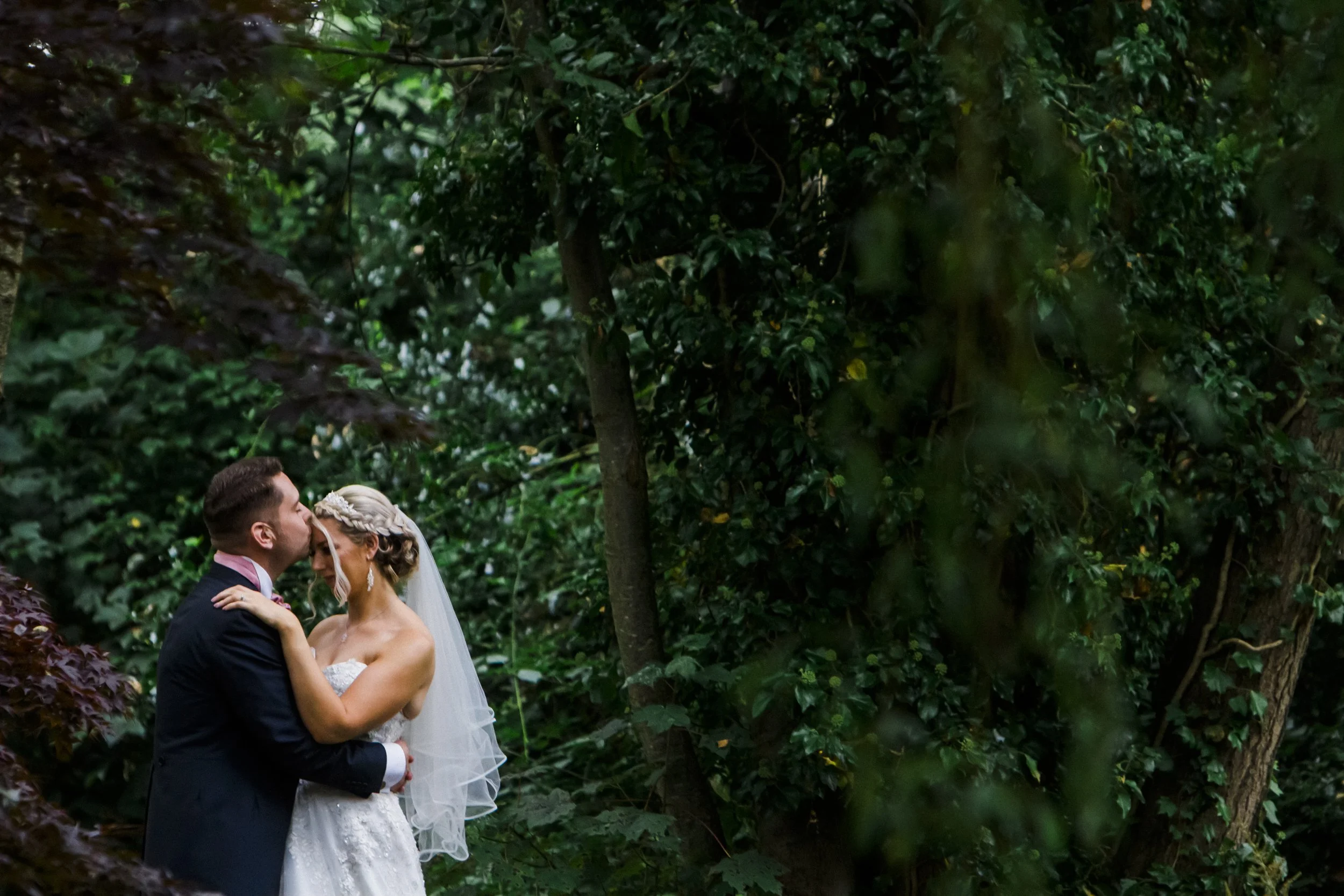 Nature's Embrace: Bride and Groom Share an Intimate Moment Surrounded by the Lush Greenery of Brook Hall Hotel