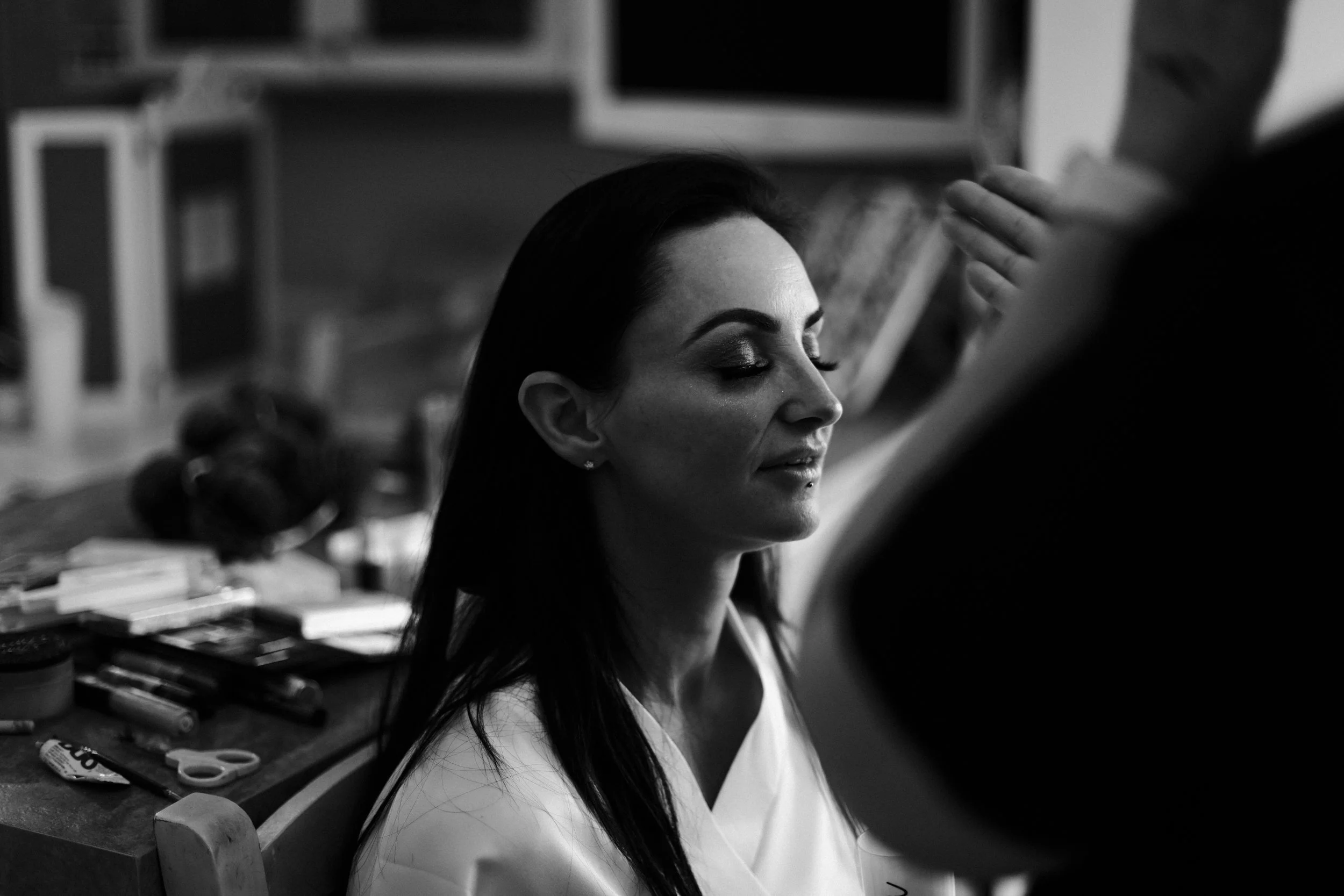 Bridal Beauty: The Bride Enjoys a Moment of Tranquility as Her Makeup Is Expertly Applied, Enhancing Her Natural Radiance for the Big Day.