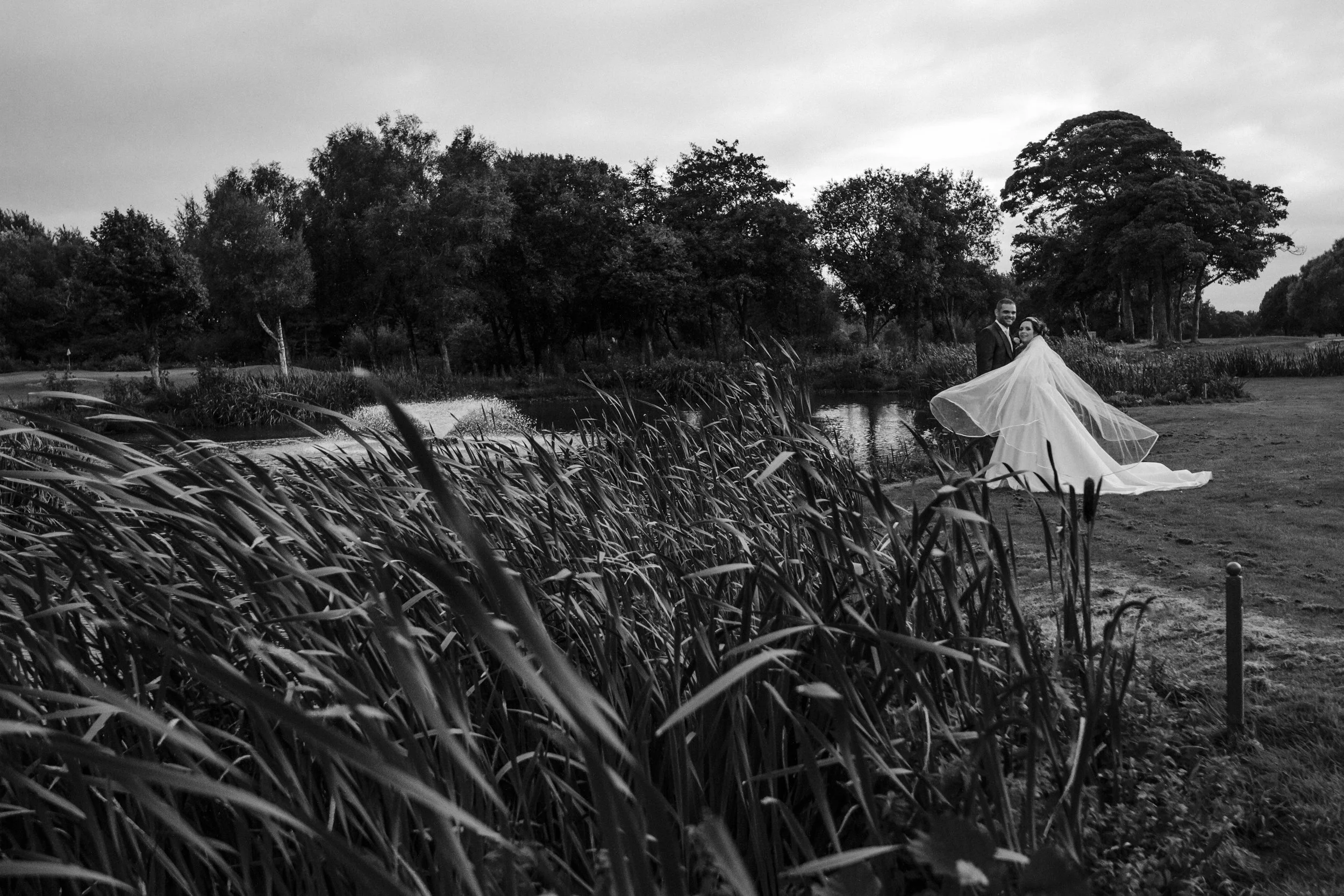 bride and groom on the grounds of Formby Hall golf course as wind blows brides veil Formby Hall Sefton Wedding Photography