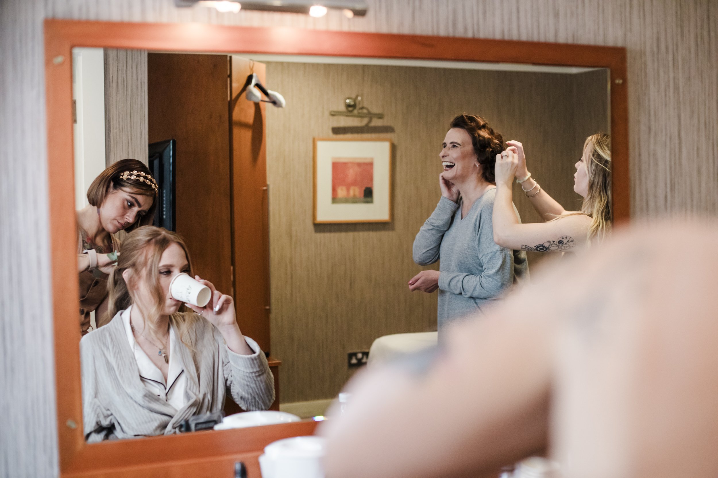 The Park Hotel Liverpool Wedding Photography: Mirror Moments of Bride's Refreshing Drink and Laughter-Filled Background