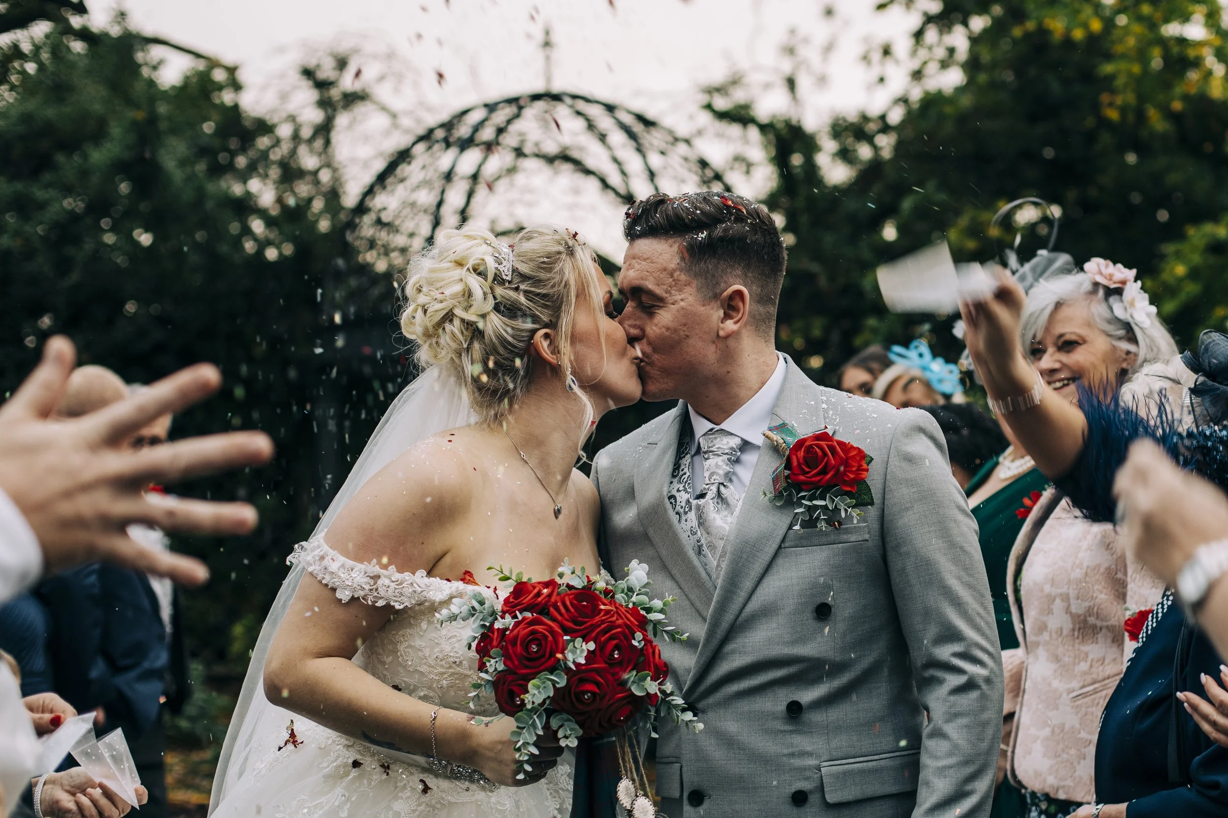 Bride and groom share a kiss at McDonald Craxton Wood Hotel amidst confetti, capturing a sweet and celebratory moment in their wedding day.