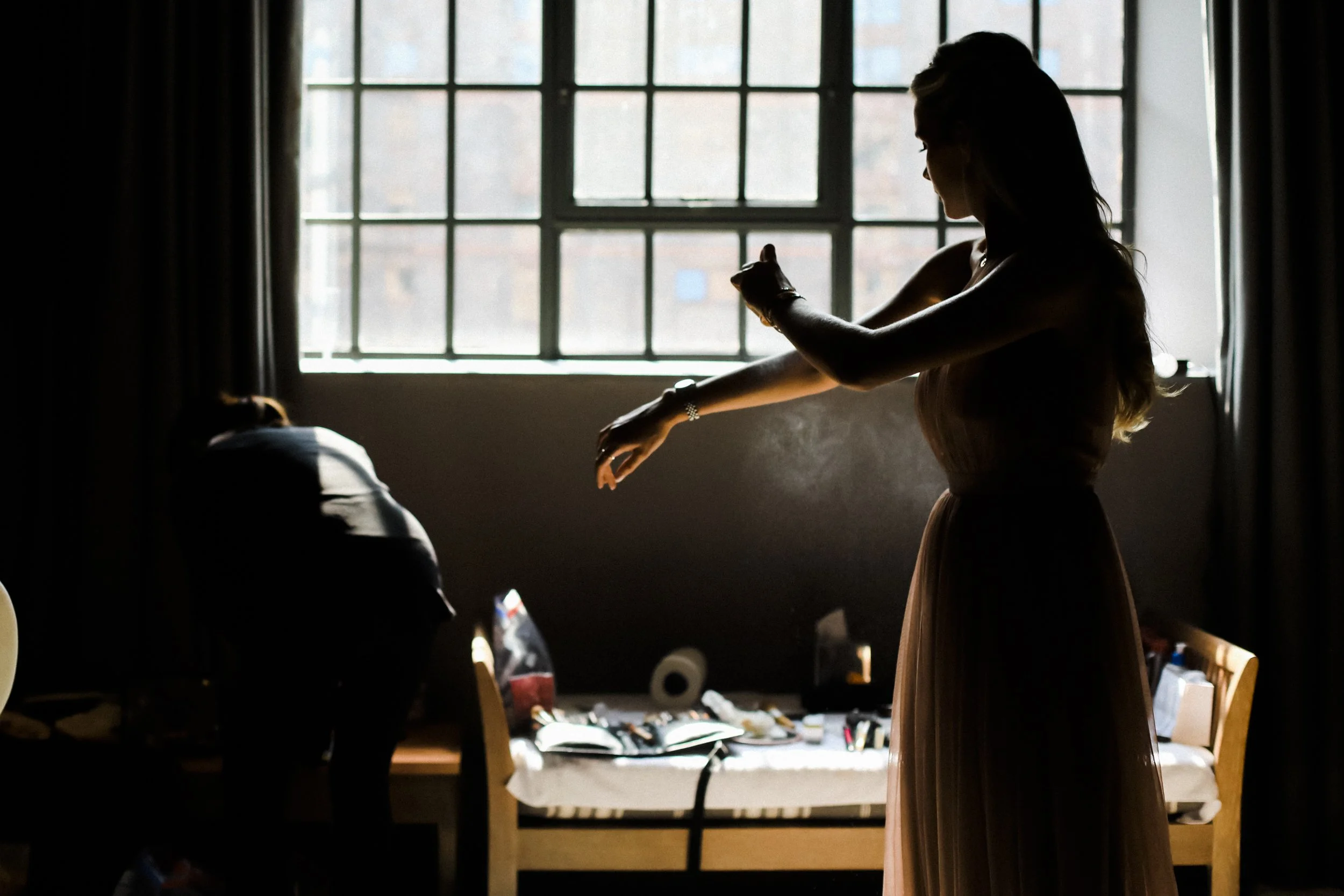 bridesmaid standing in front of the window at the Titanic hotel spraying perfume. Liverpool Wedding Photographers