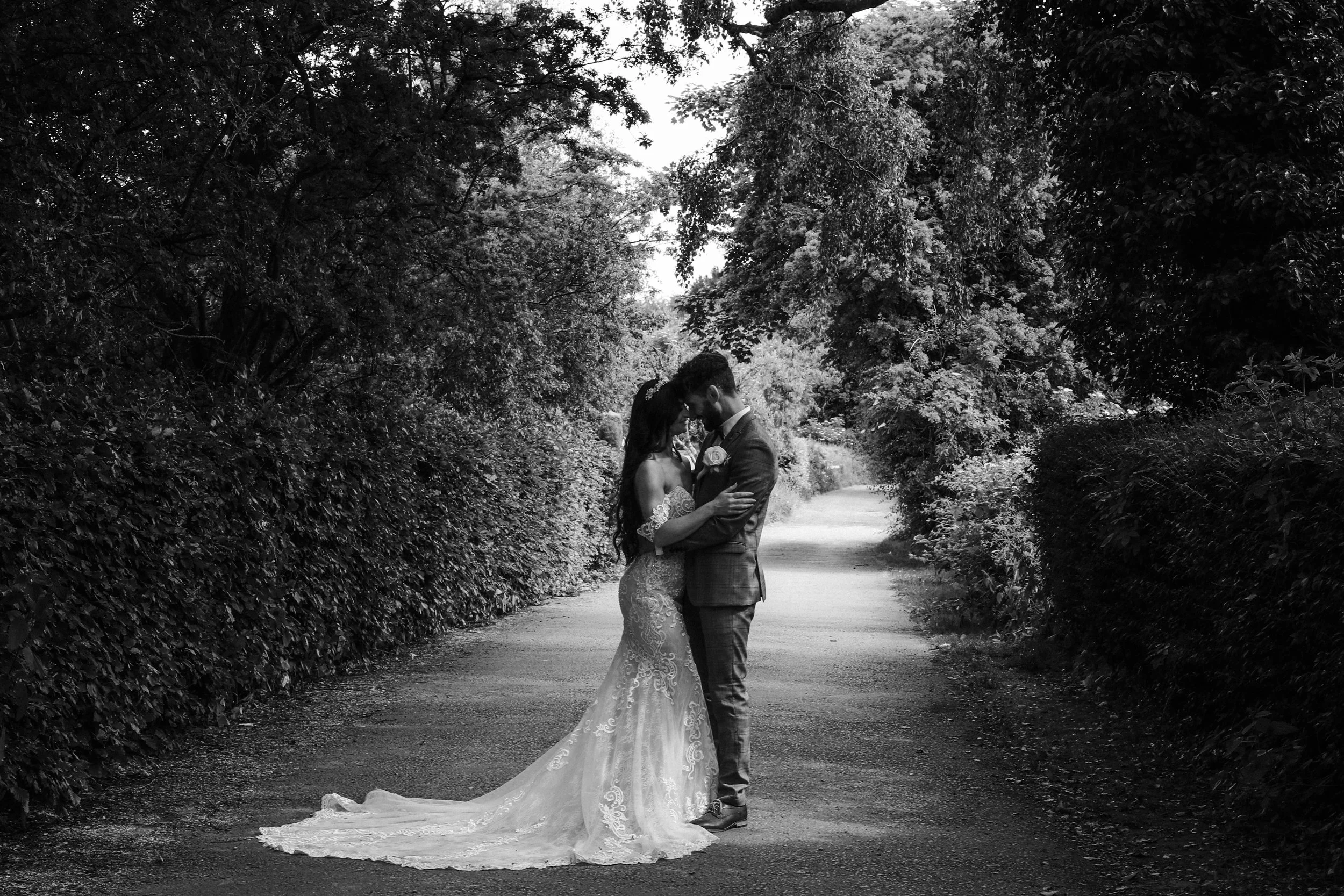Liverpool wedding photography, the bride and groom embrace amidst lush greenery, captured in a timeless black and white composition. A beautifully serene moment frozen in monochrome elegance