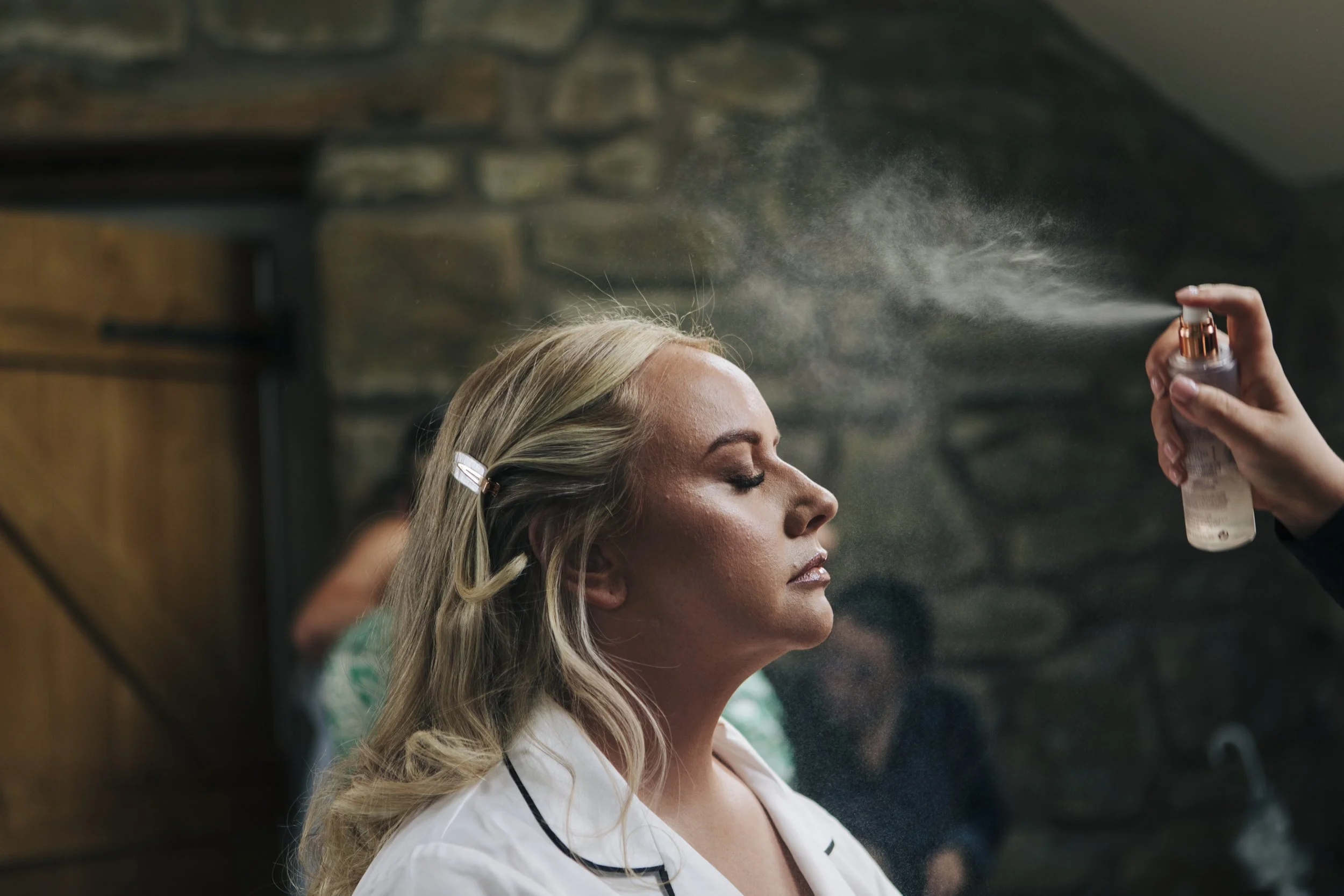 Bride, mid-mist of setting spray at Tower Hill Barns, exudes elegance and confidence during makeup preparation. A poised moment capturing her elegant and confident look in the making