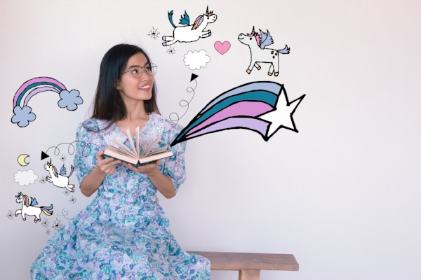 Young asian woman reading A fairy tales book with unicorn and rainbow illustration doodles- imagination concept