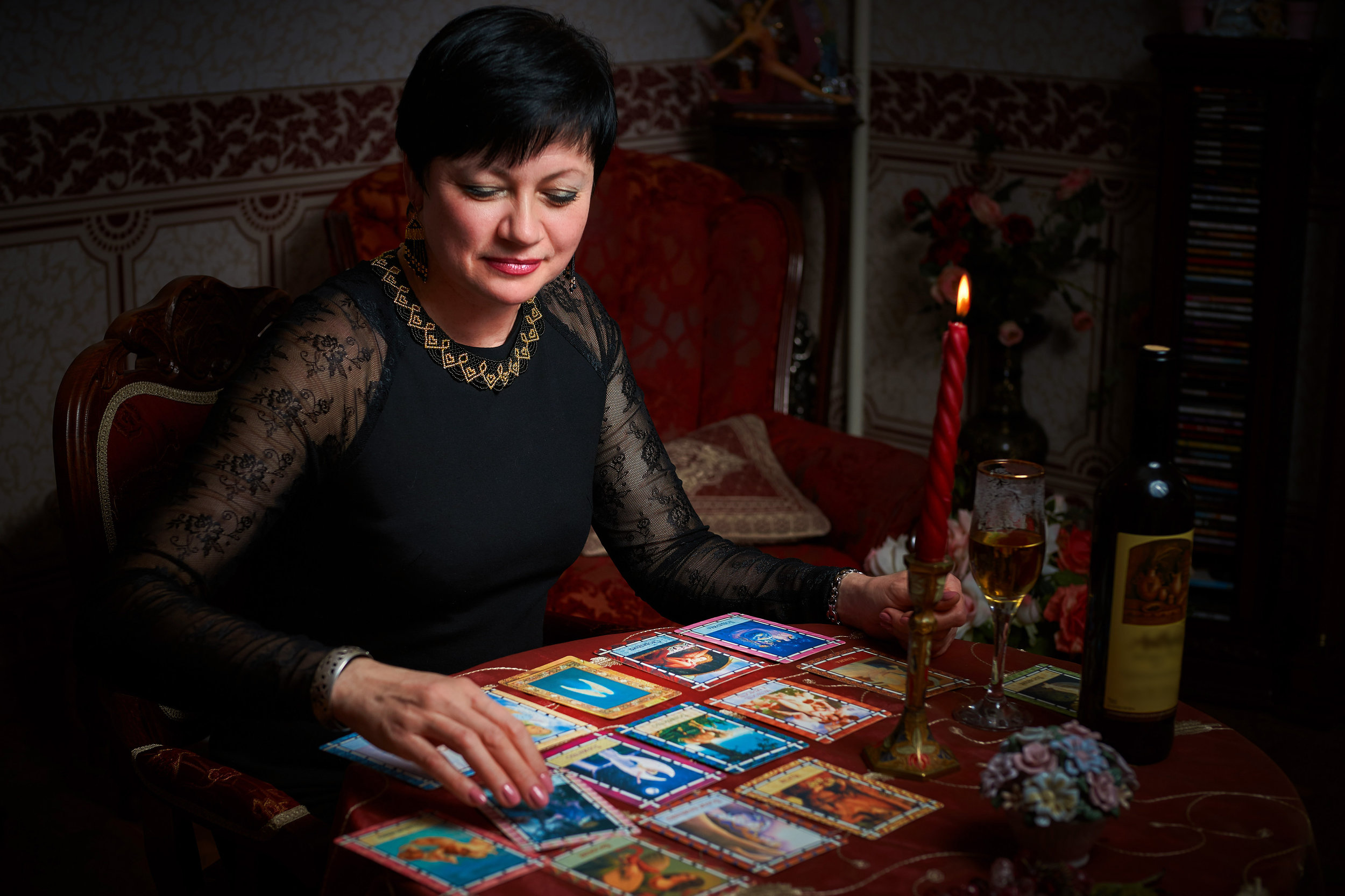 Fortune teller woman reading tarot cards in the dark room with a glass of wine