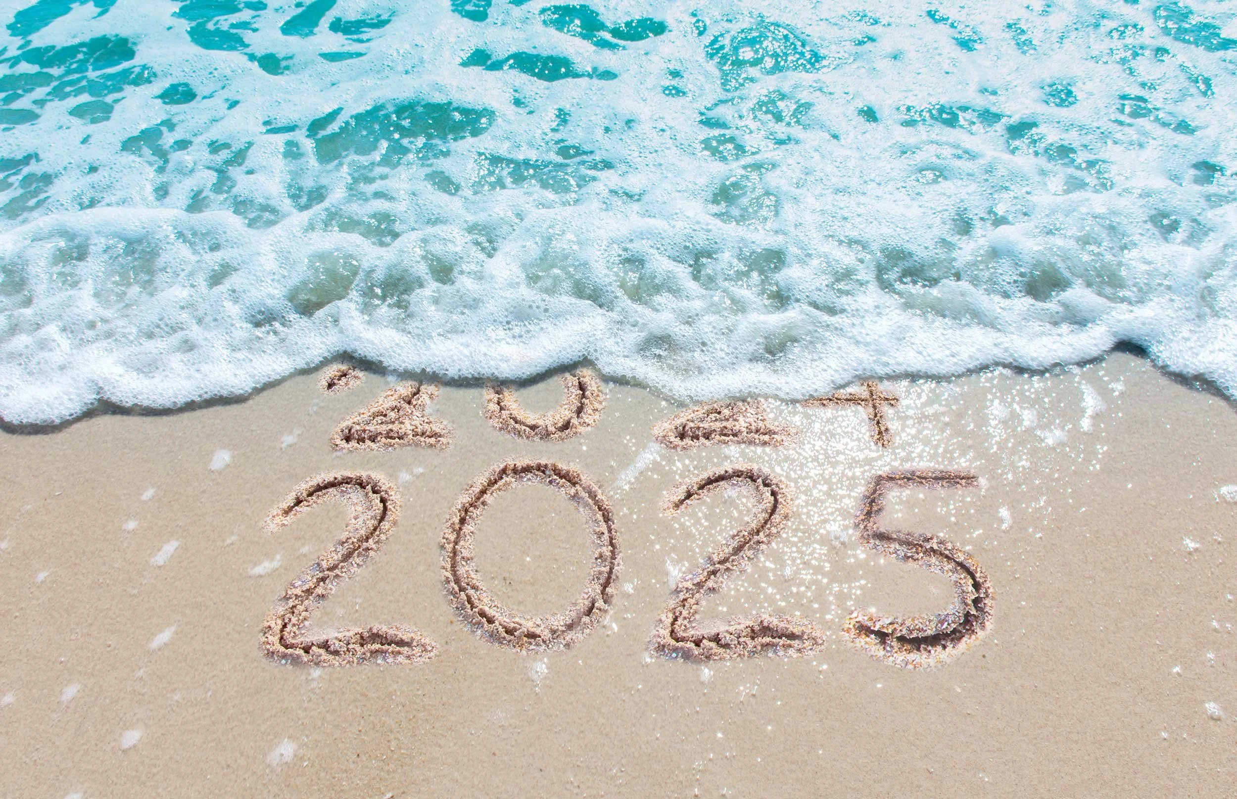 2025 is written in the sand, as a wave washes away 2024.