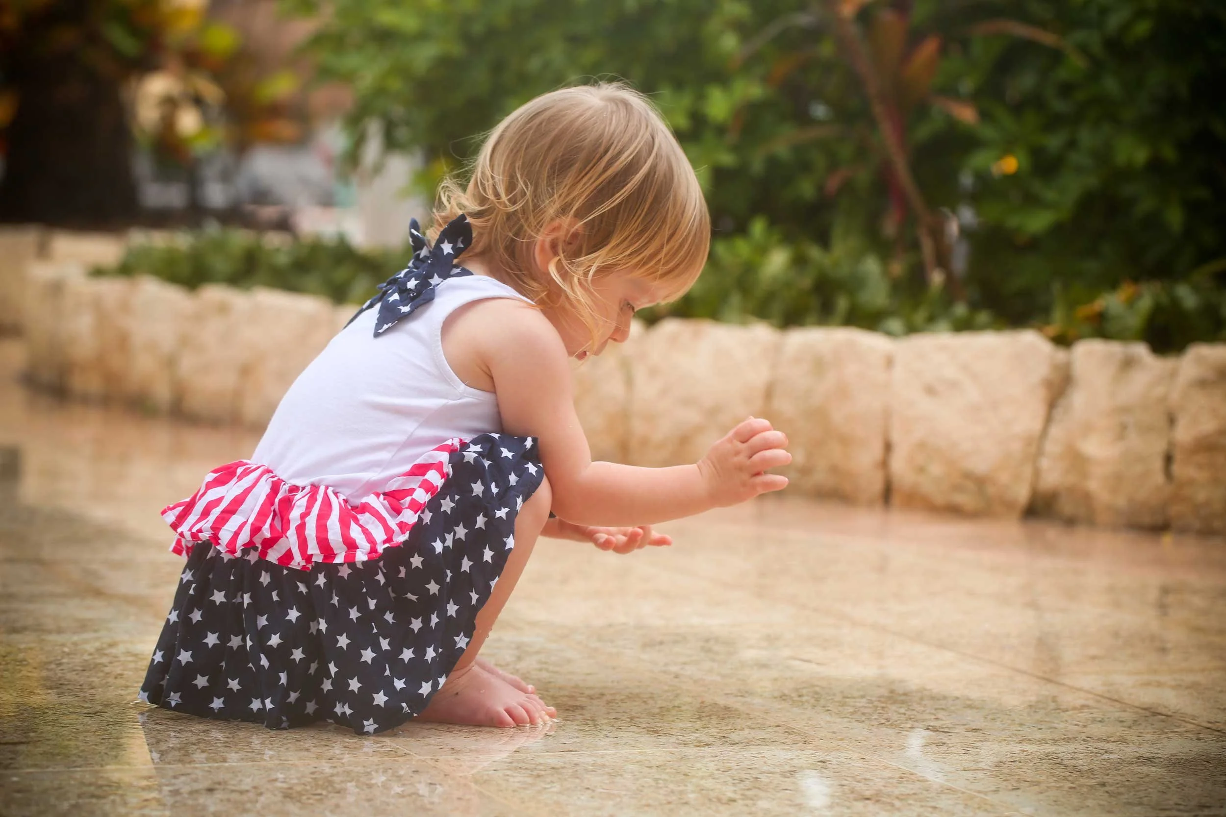 A young child dressed for Independence Day celebrations crouches to examine a garden path.