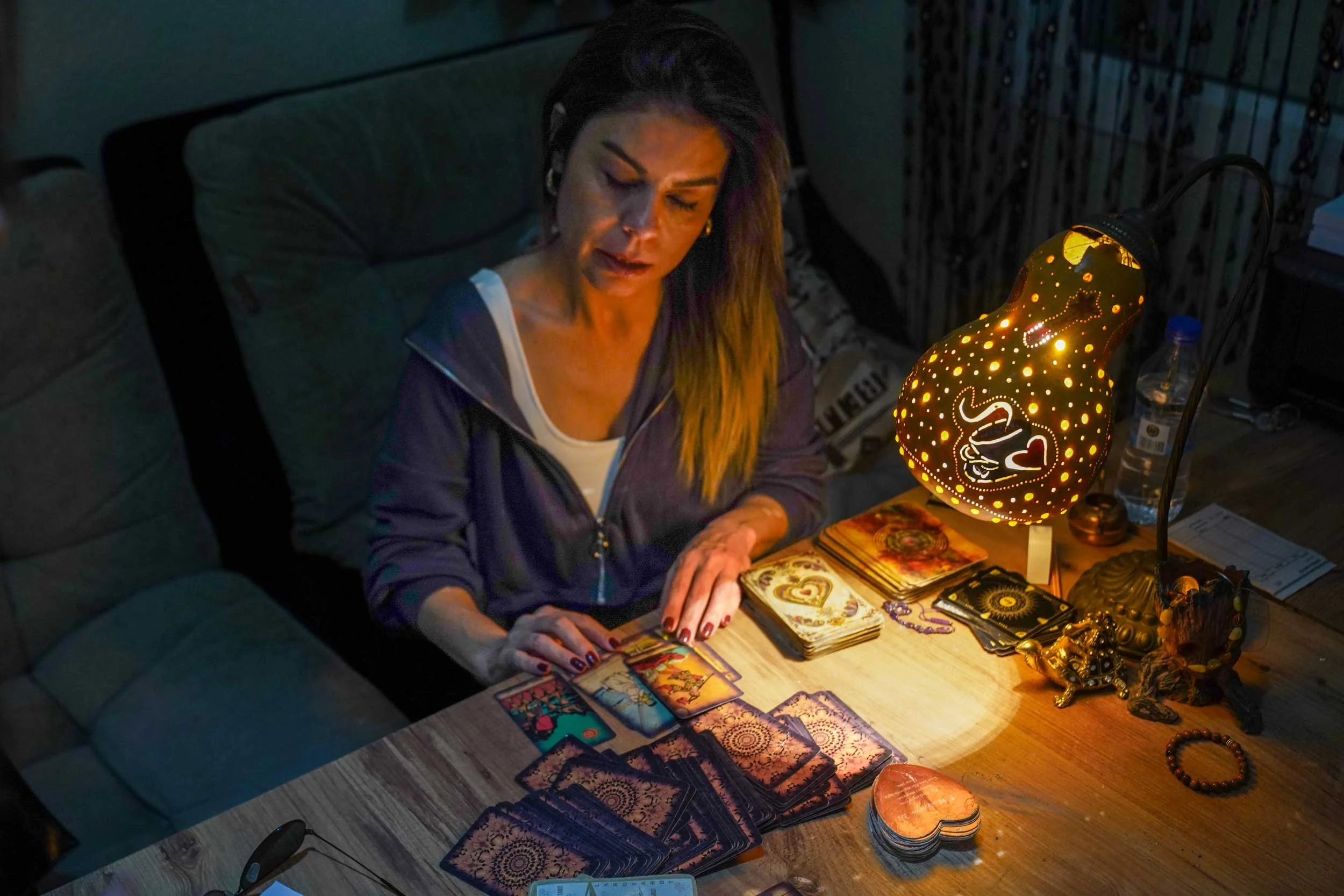 A woman reading her cards under a desk lamp in a dimly lit room.