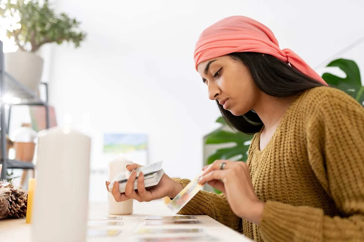 Close up of a woman reading tarot cards with candles at home.