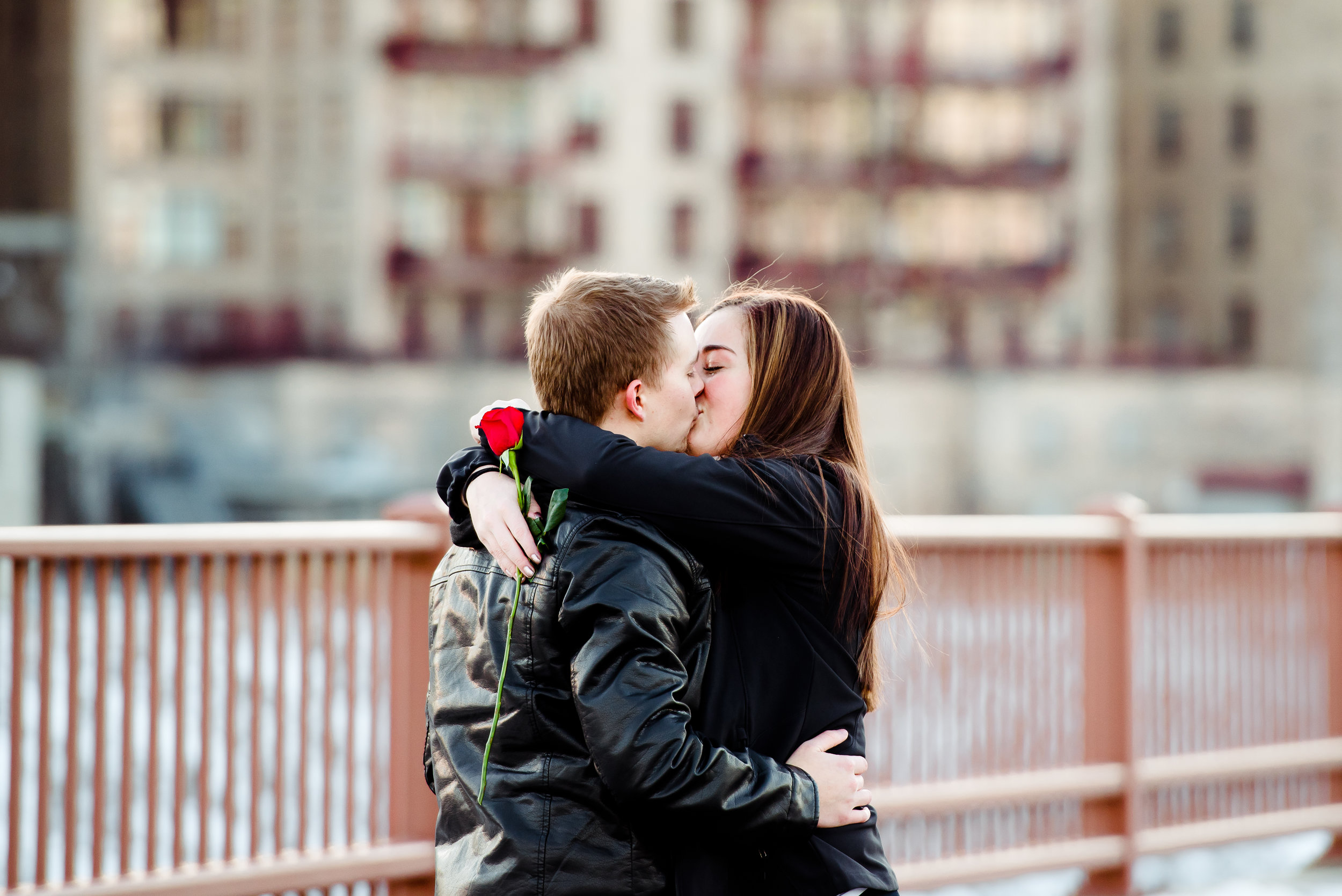 Marriage Proposal on the Stone Arch Bridge in Minneapolis - Romantic Kiss with Single Red Rose - Winter Engagement Minneapolis Proposal Photographer