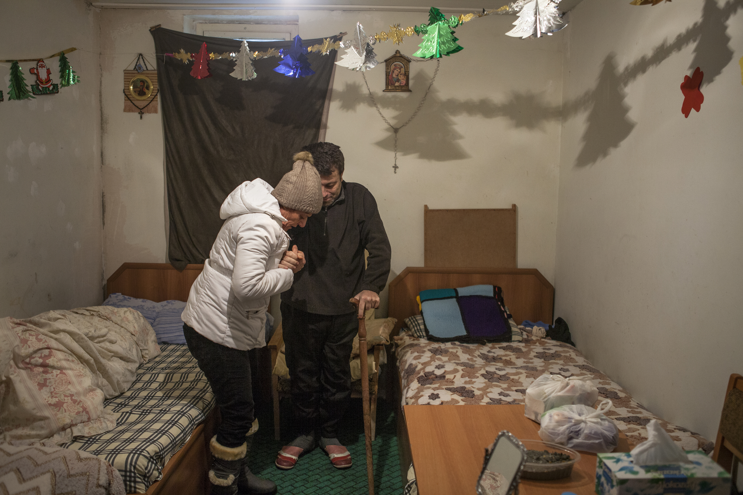  A displaced Syrian-Armenian helps her bedridden adult son walk to the bathroom in a house provided by the Catholic Church for Syrian-Armenians with the most need for assistance. 