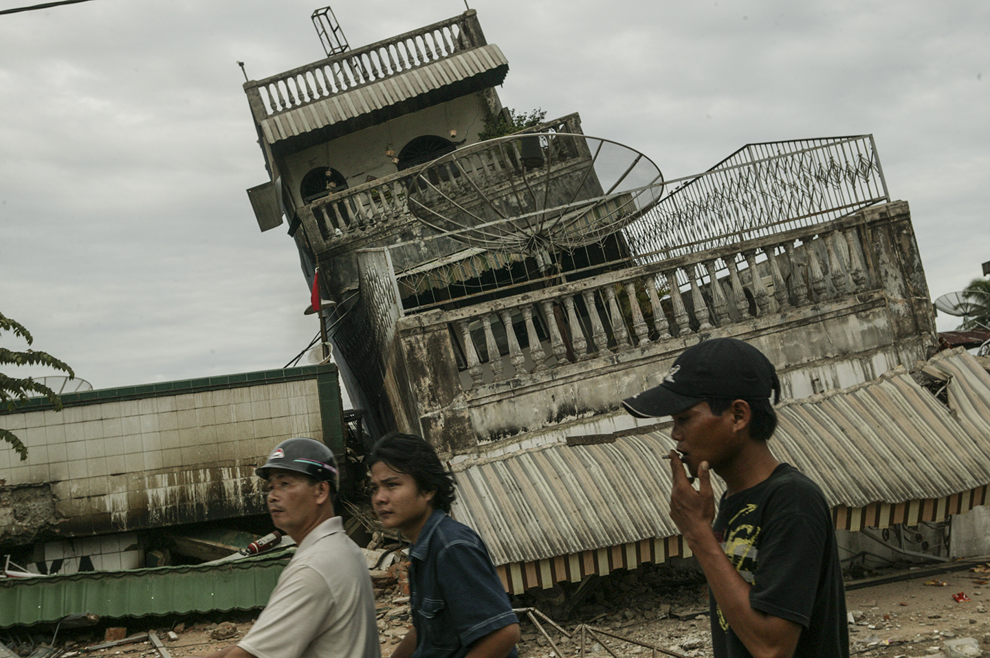  Locals ride by a collapsed building. 