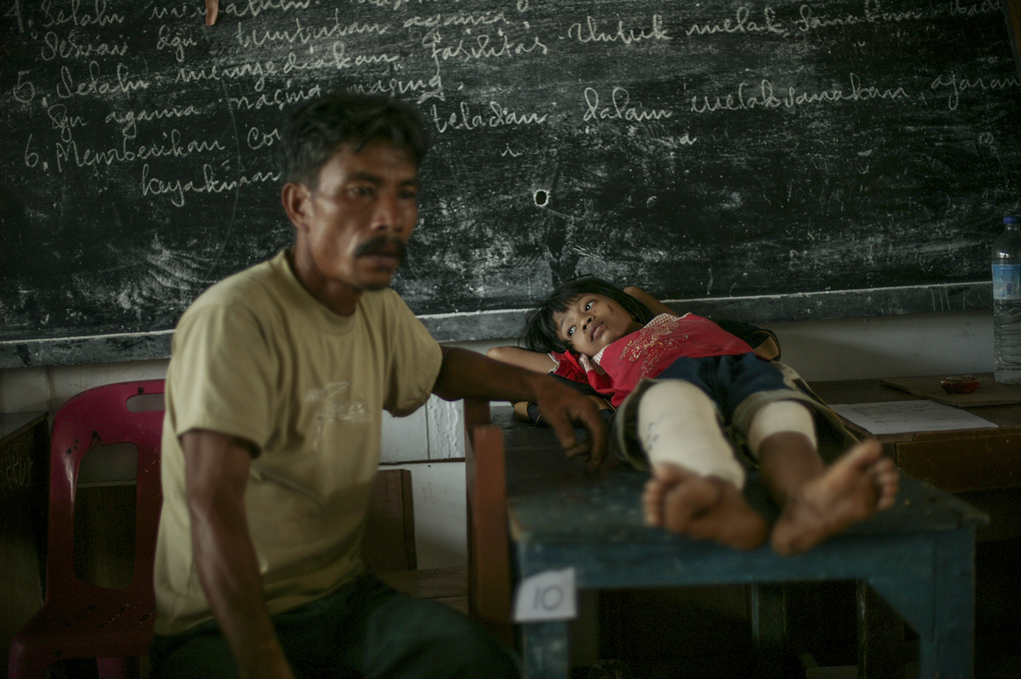 A father next to his injured daughter at a makeshift hospital where they wait to be evacuated. 