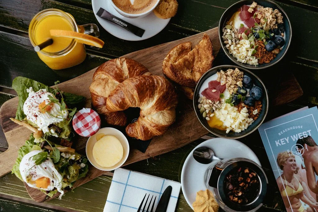 Ontbijtbord met croissants, toast, salad met eitje, yoghurt met muesli en bessen, een glas sinaasappelsap, koffie, en een glas cola