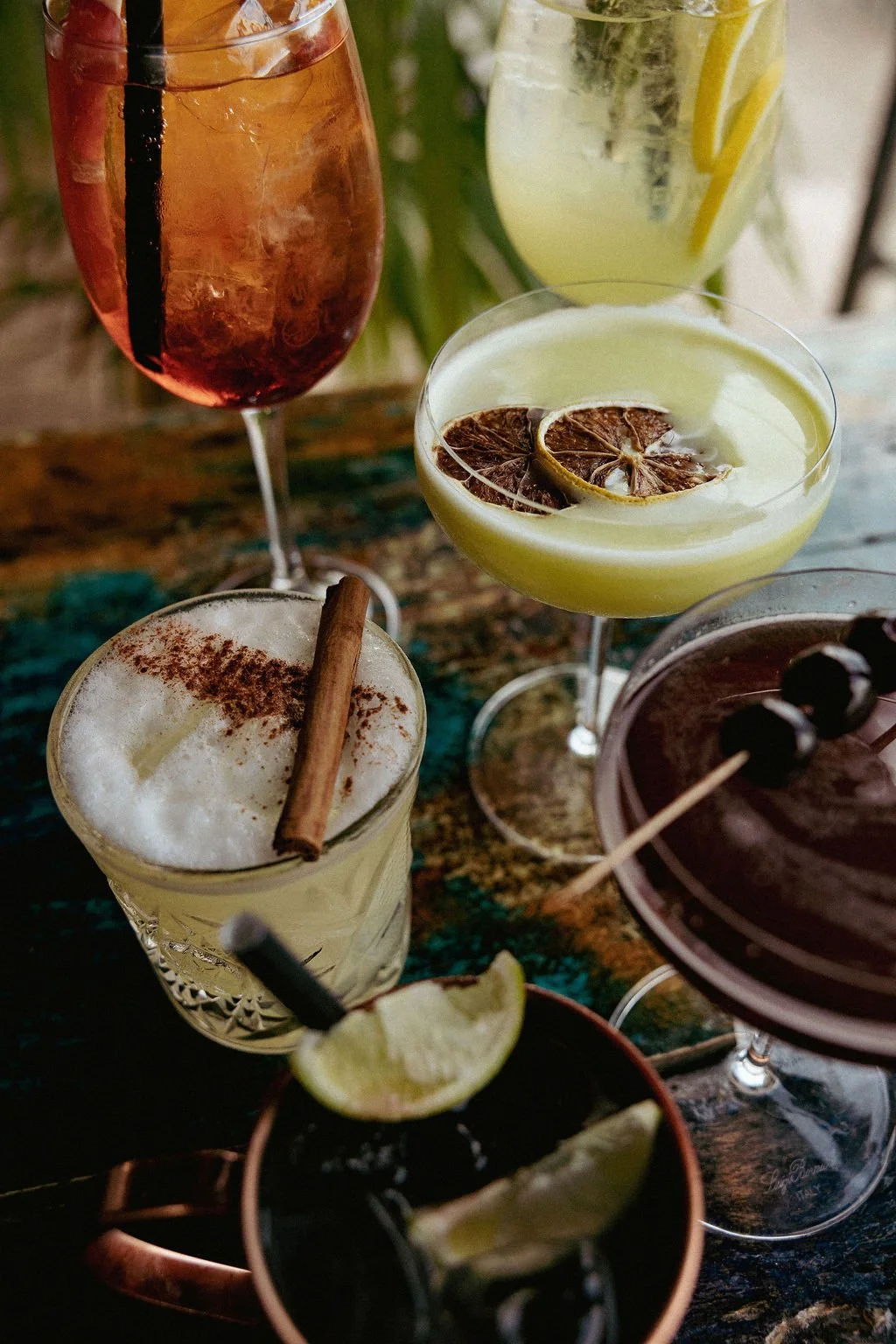 Verschillende cocktails op een tafel, met citroen-, limoen- en andere garnituren, waaronder een cocktail met een kaneelstokje en een schijfje citroen.