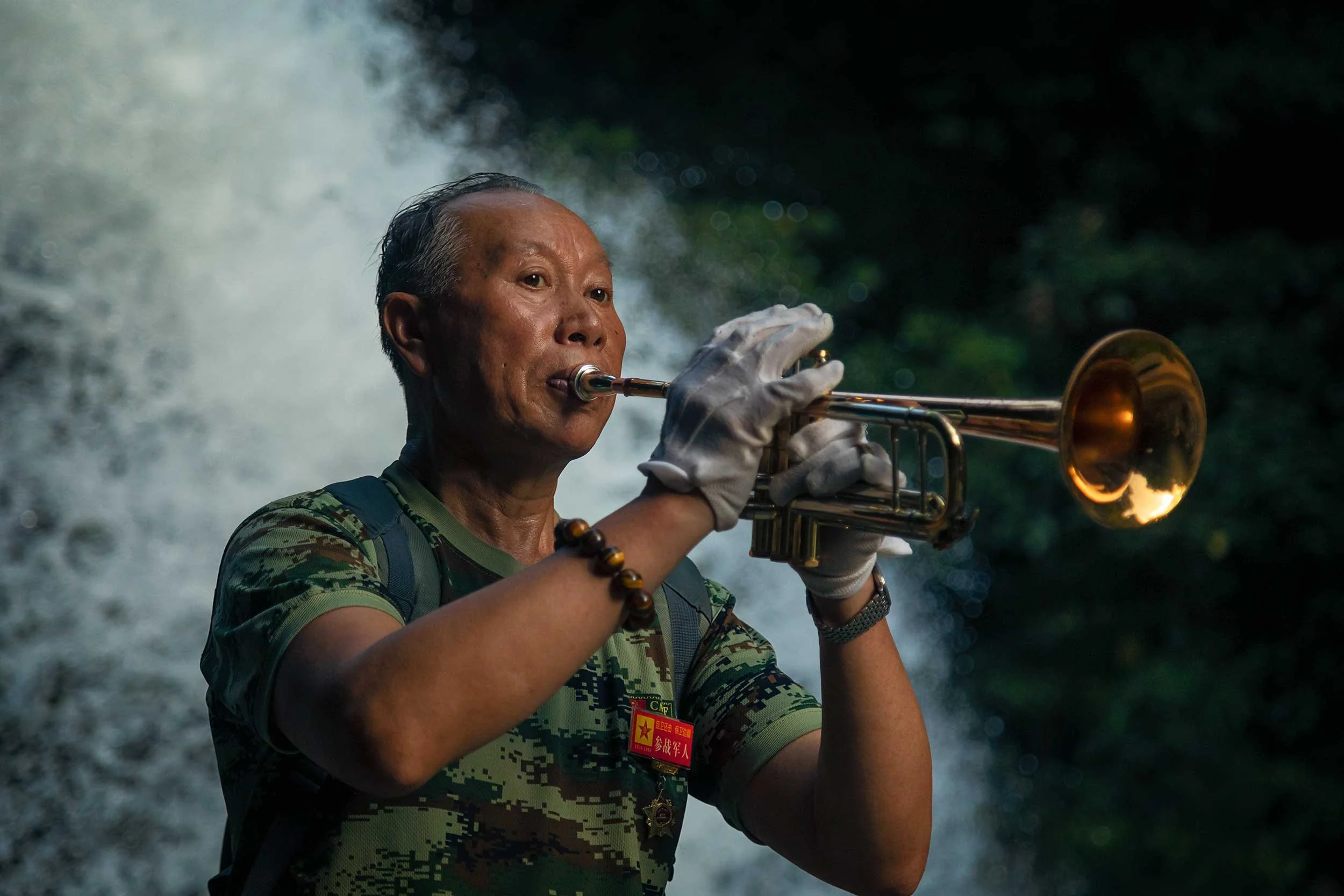 Portrait of elderly chinese man playing a trumpet in front of waterfall.