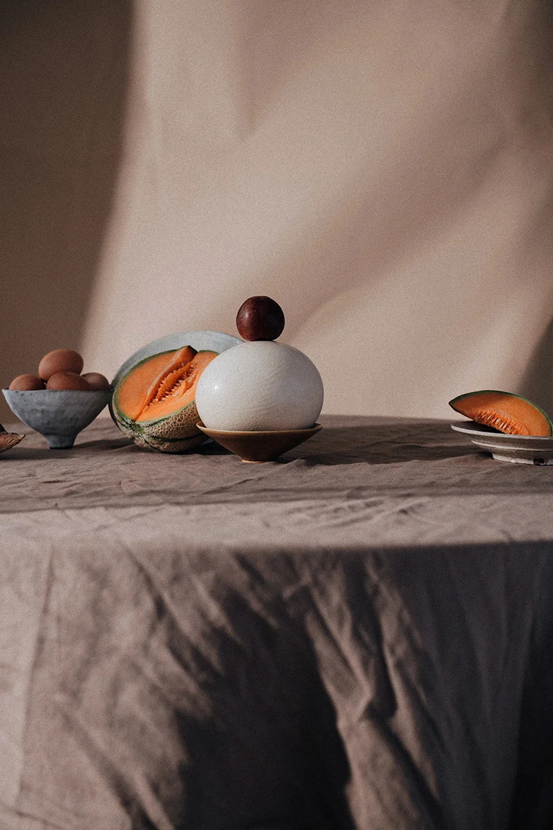 Still life photograph for In Bed Linen editorial studio featuring fruit and pottery on a tabletop.