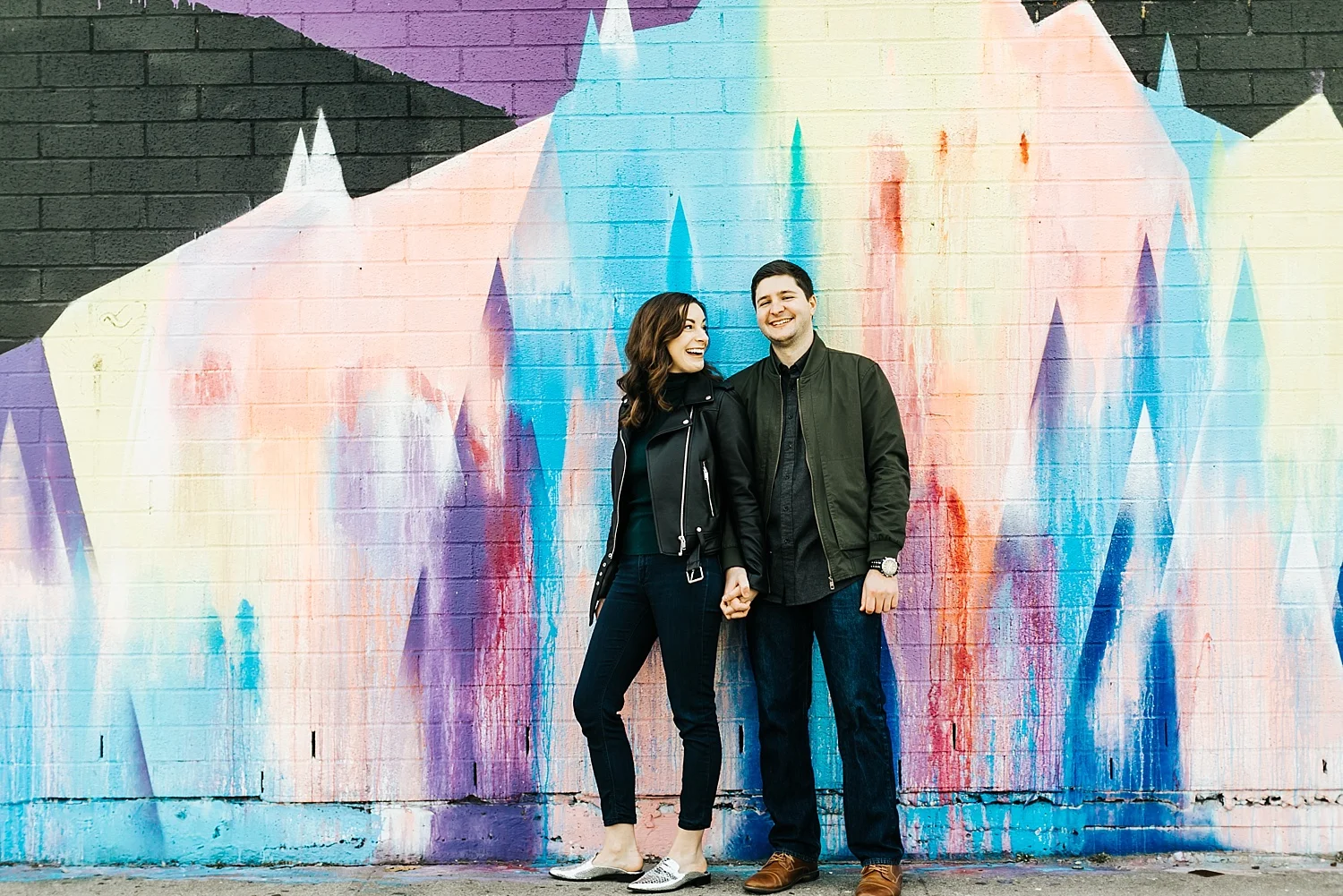 A couple holding hands in front of a mural in Brooklyn, NYC.