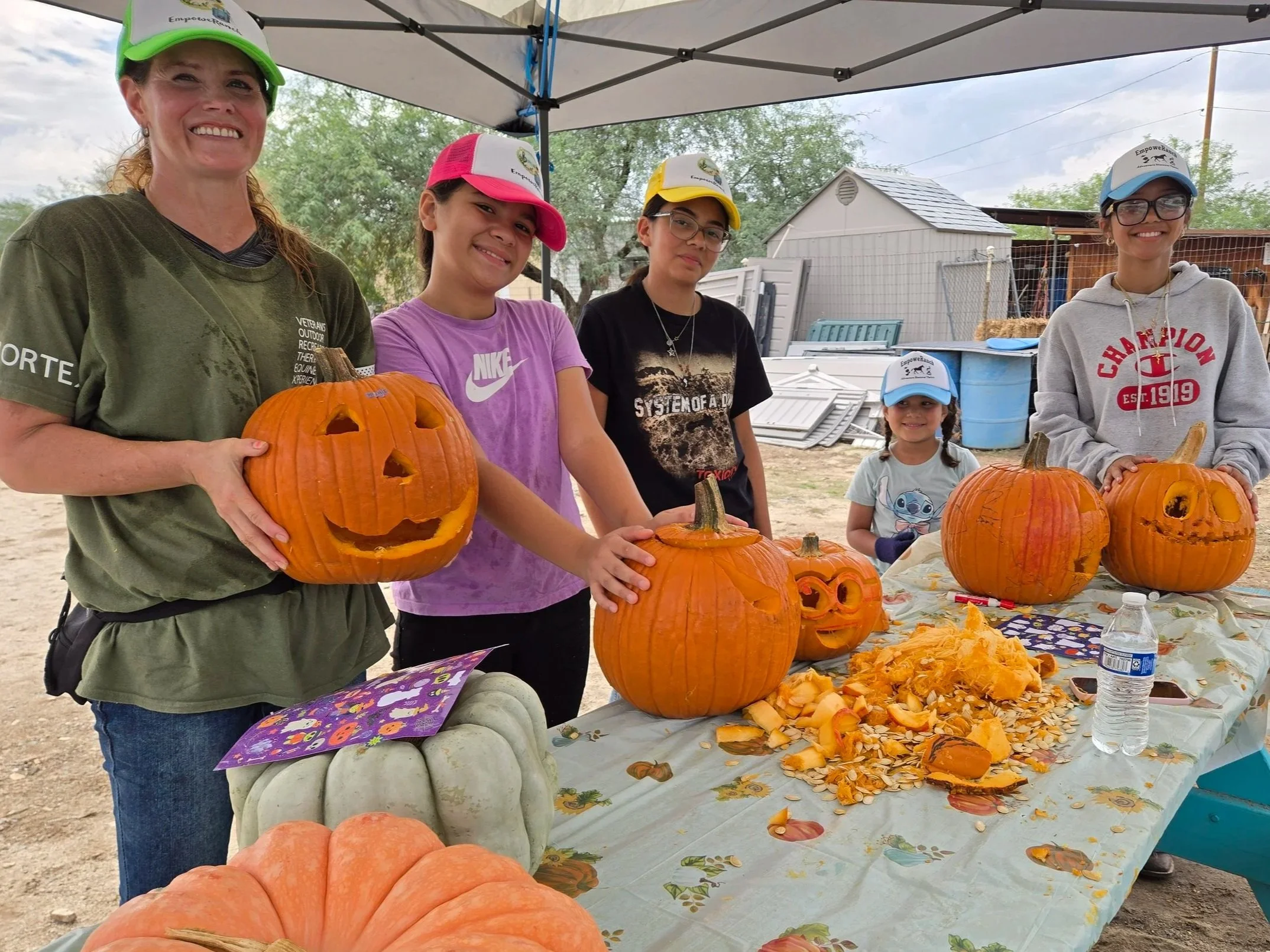 EmpoweRanch campers and a team member smiling beside pumpkins they carved during fall camp