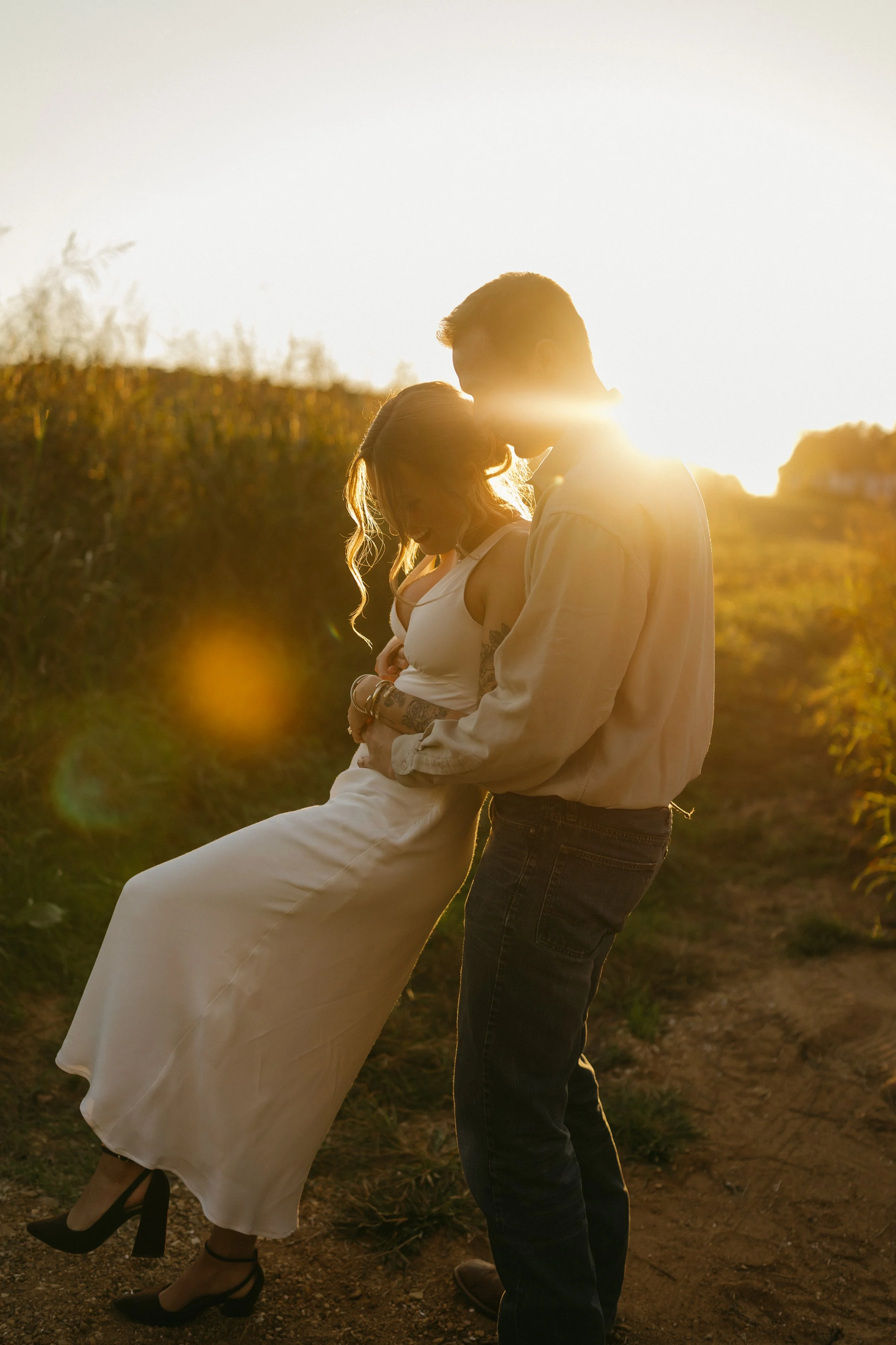 A couple sharing a romantic moment outdoors during sunset, standing close and kissing.
