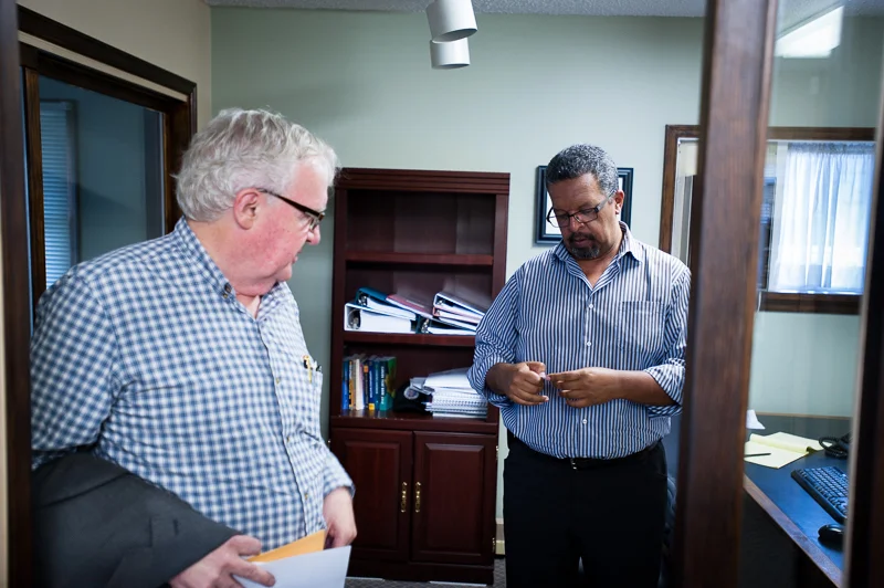 David McKenzie and Aklilu Mulat, the executive director at HOPE International Development Agency, study my business card. Aklilu came to study in Canada from Ethiopia in 1979, only 17 years old. Now, a seasoned Canadian, he reaches out across nations to help people in Ethiopia and all over the world. At HOPE International office, New Westminster, BC, Canada on August-15-2013. Photo: Art Zaratsyan