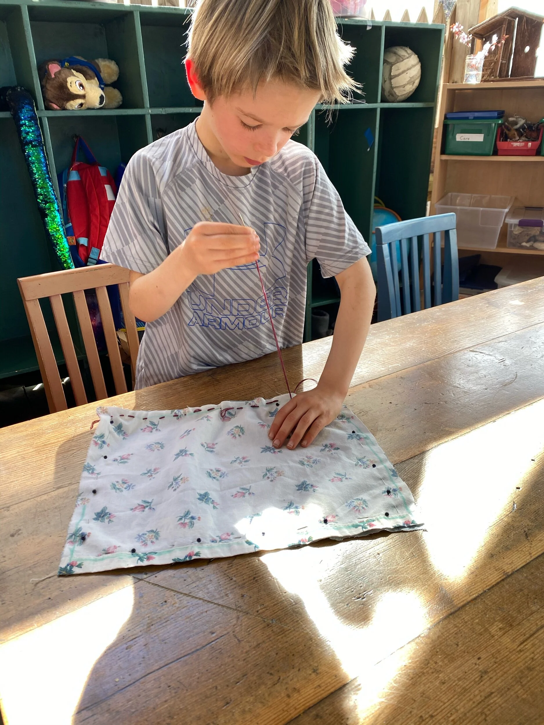 Students have been working on sewing a pillow for rest time. A few are finished. All are progressing impressively with their fine motor skills and concentration as you can clearly see in this series  — titled: Boys Who Sew Well.